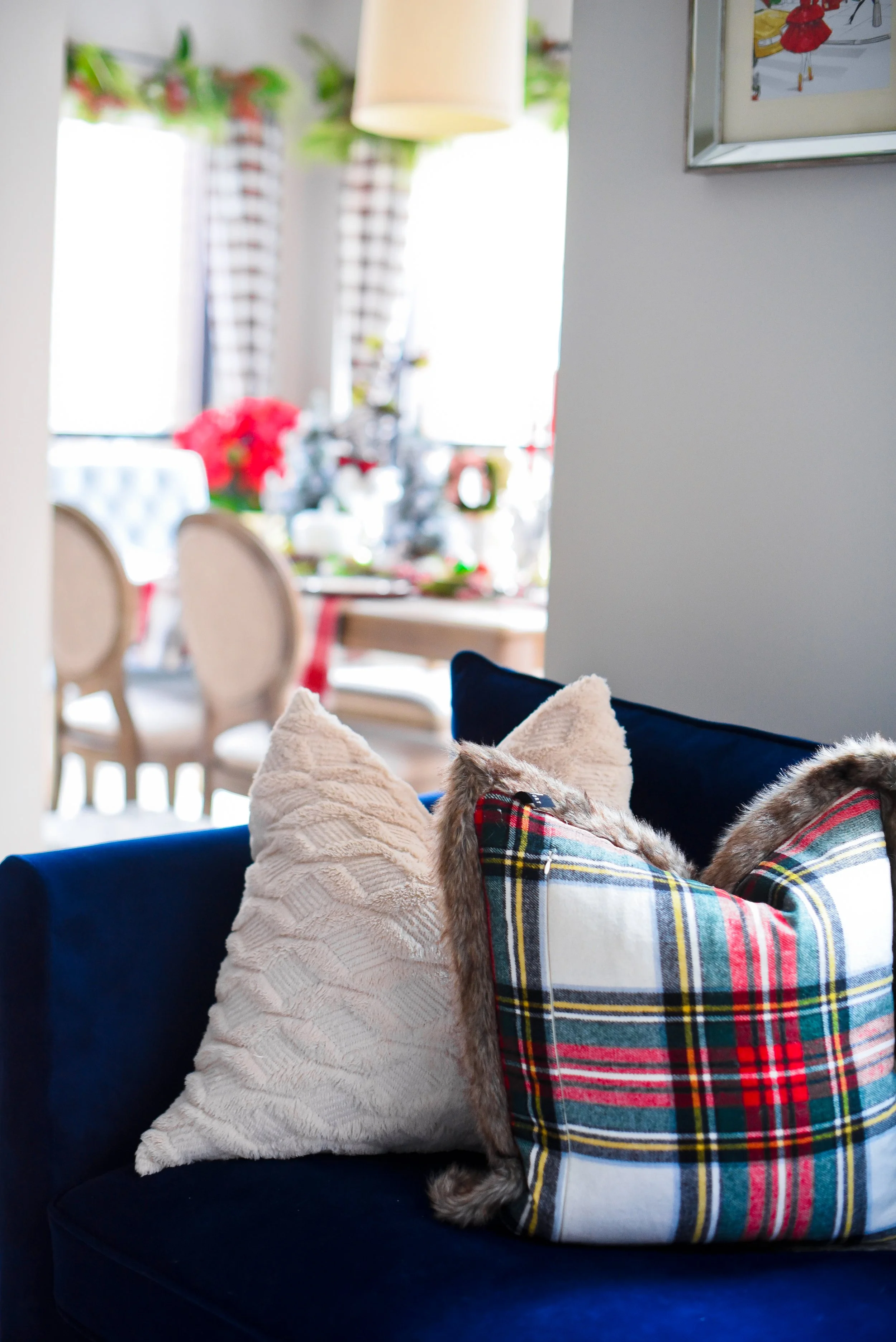 Living room with a navy blue sofa adorned with beige and plaid pillows, with a dining area decorated for Christmas visible in the background.