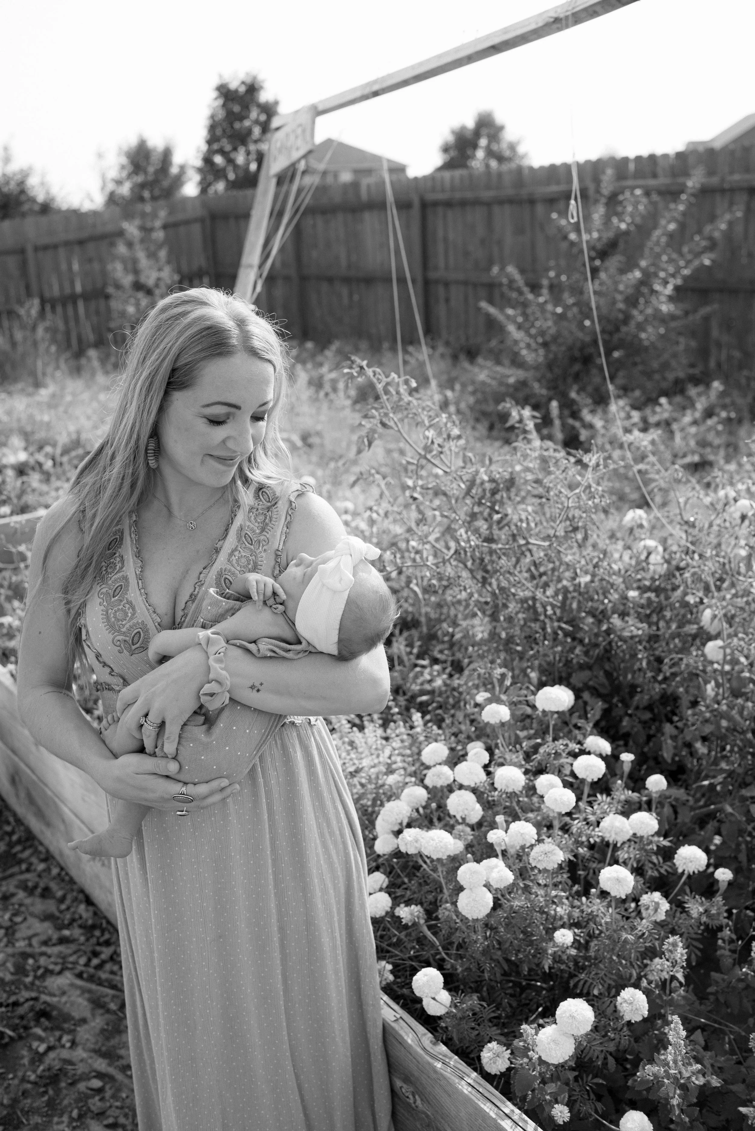 A woman holding a baby in a garden, with flowers and trees in the background, in black and white.