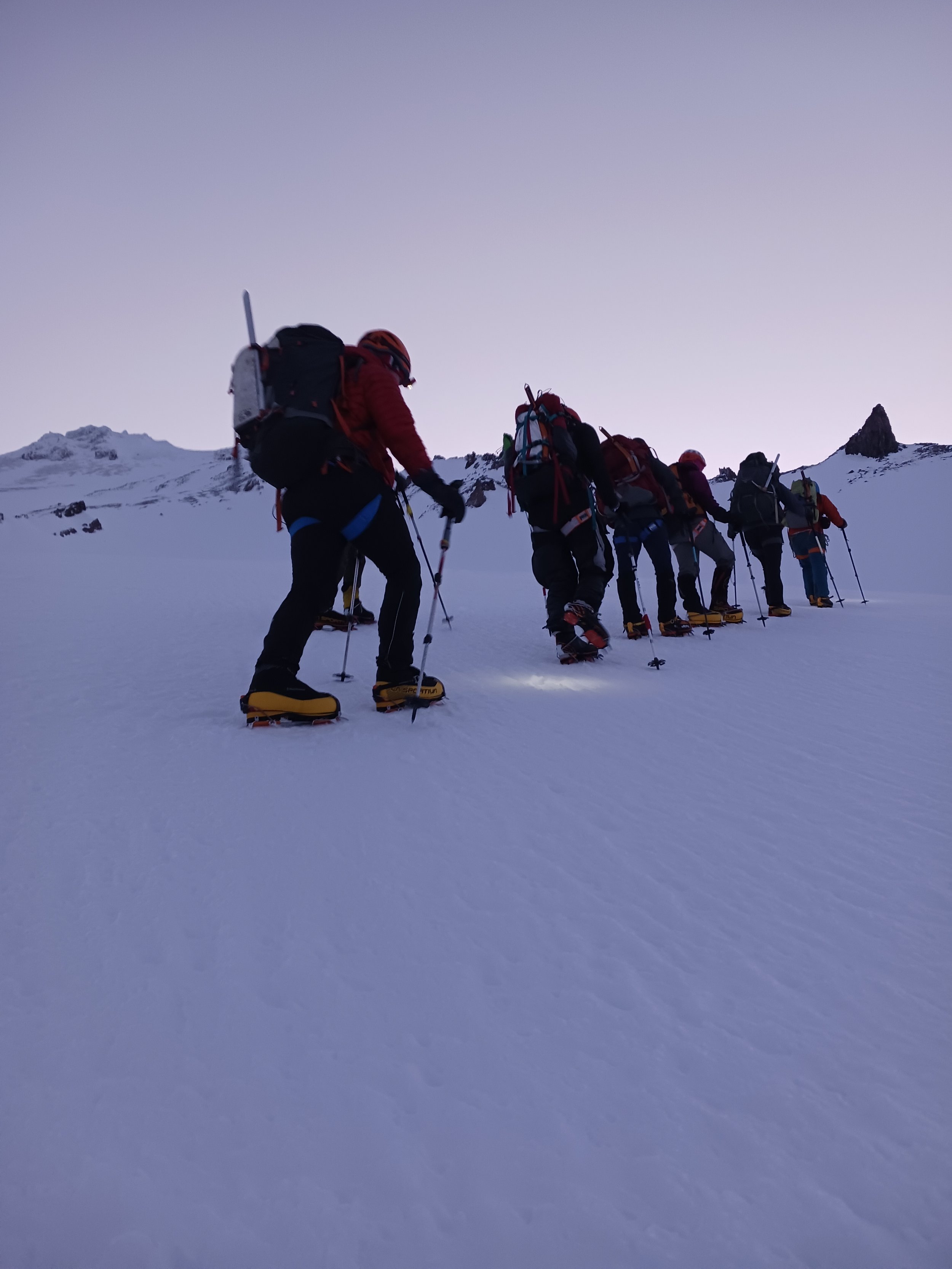 Group of climbers in snow, ascending a mountain with snow boots, poles, and backpacks