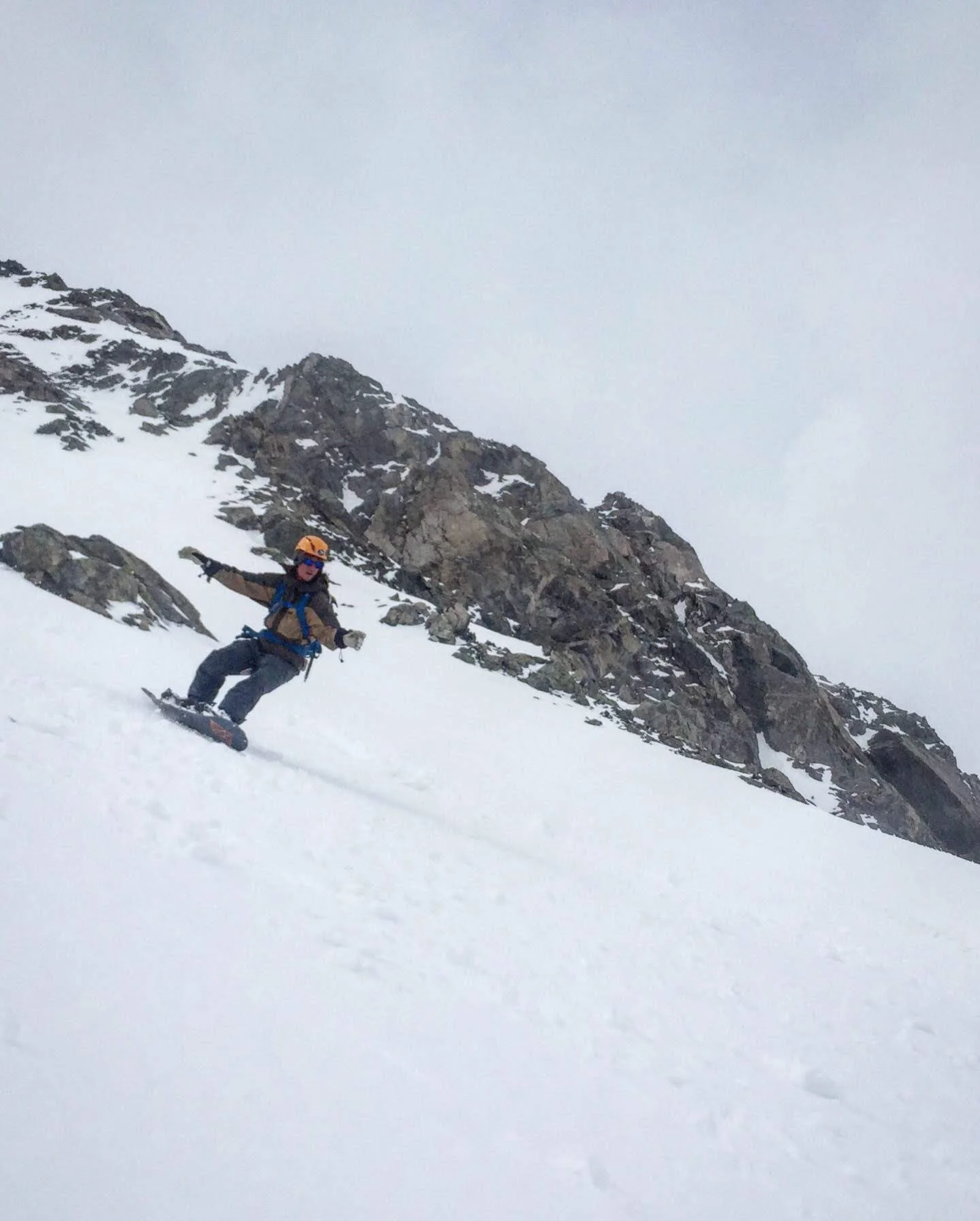 Person snowboarding on a snowy mountain slope with rocks in the background.