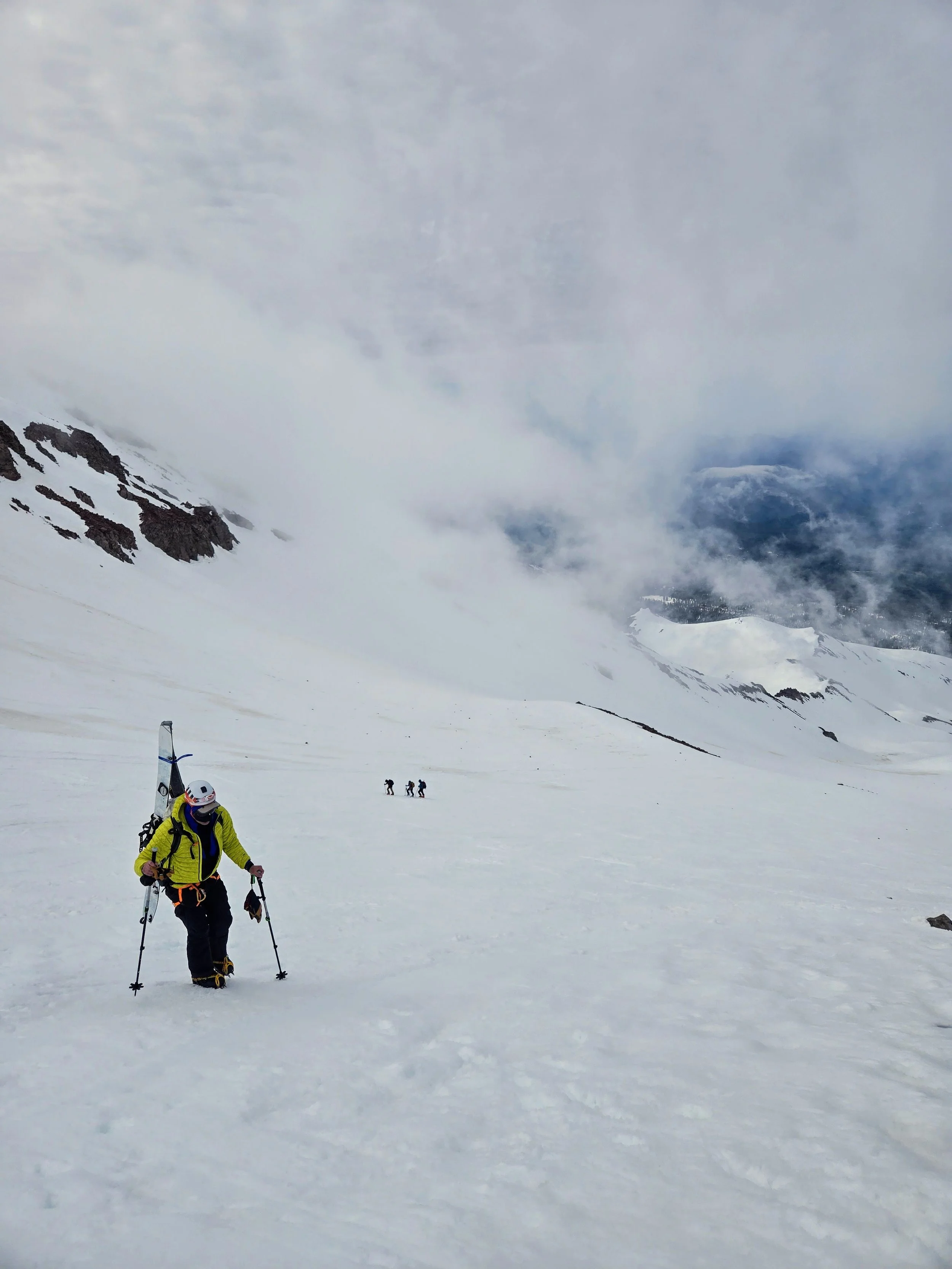 A group of climbers on a snow-covered mountain with cloudy skies and rocky outcroppings in the background.