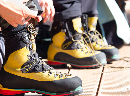 Close-up of two people wearing yellow and black hiking boots on a wooden dock.