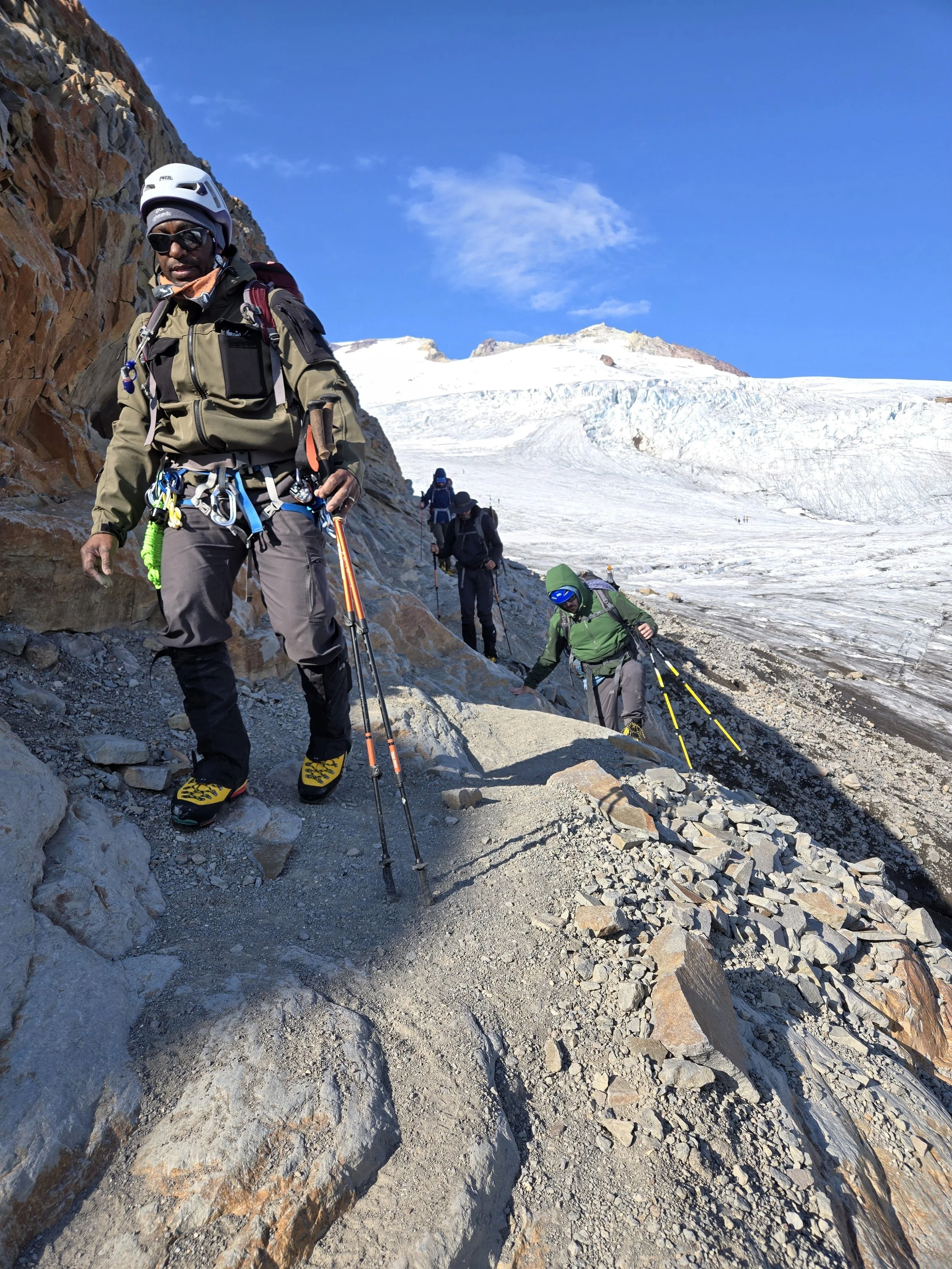 A group of mountaineers ascending a rocky and icy mountain slope with snow and glacier in the background.