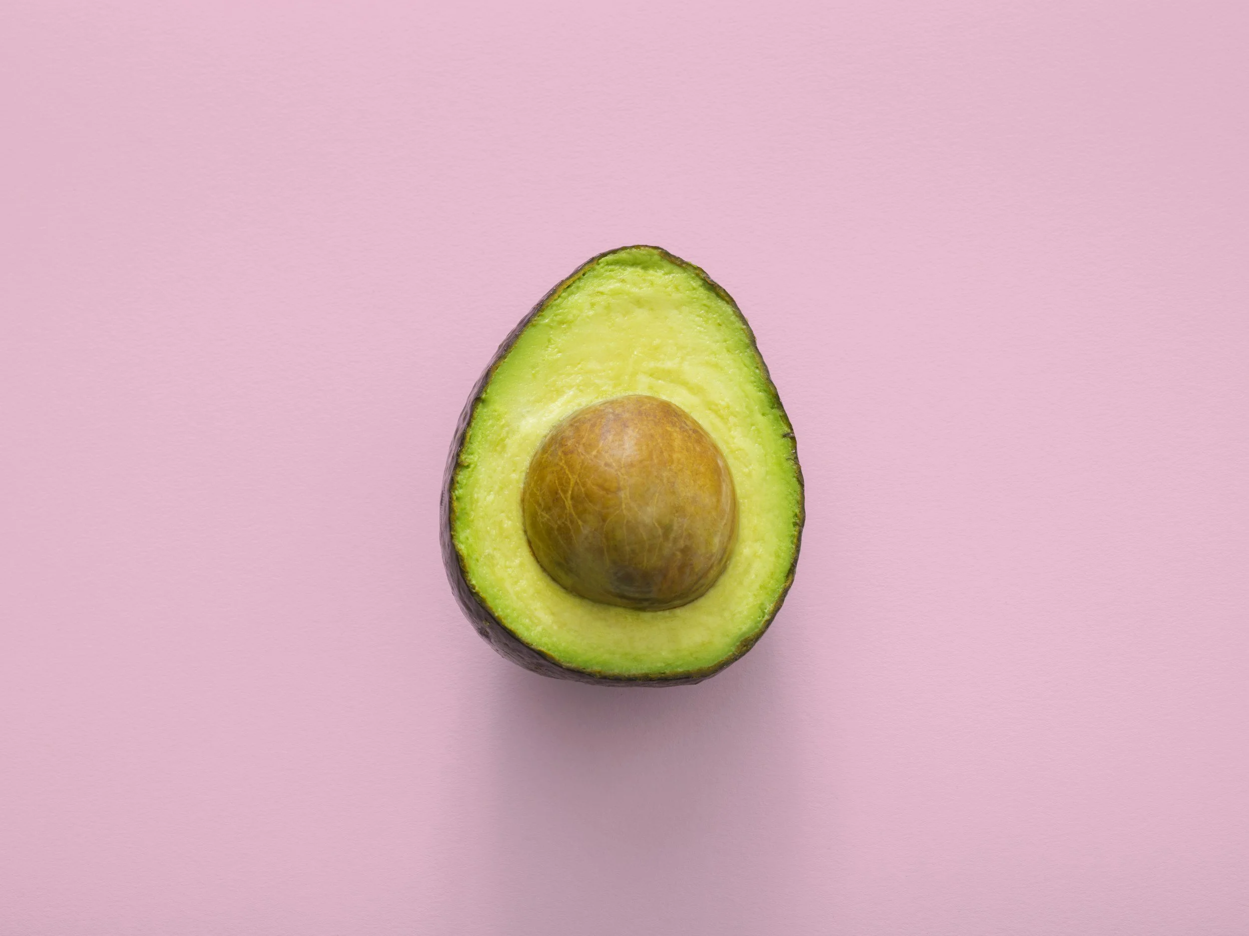 A sliced avocado with seed, placed on a pink background.