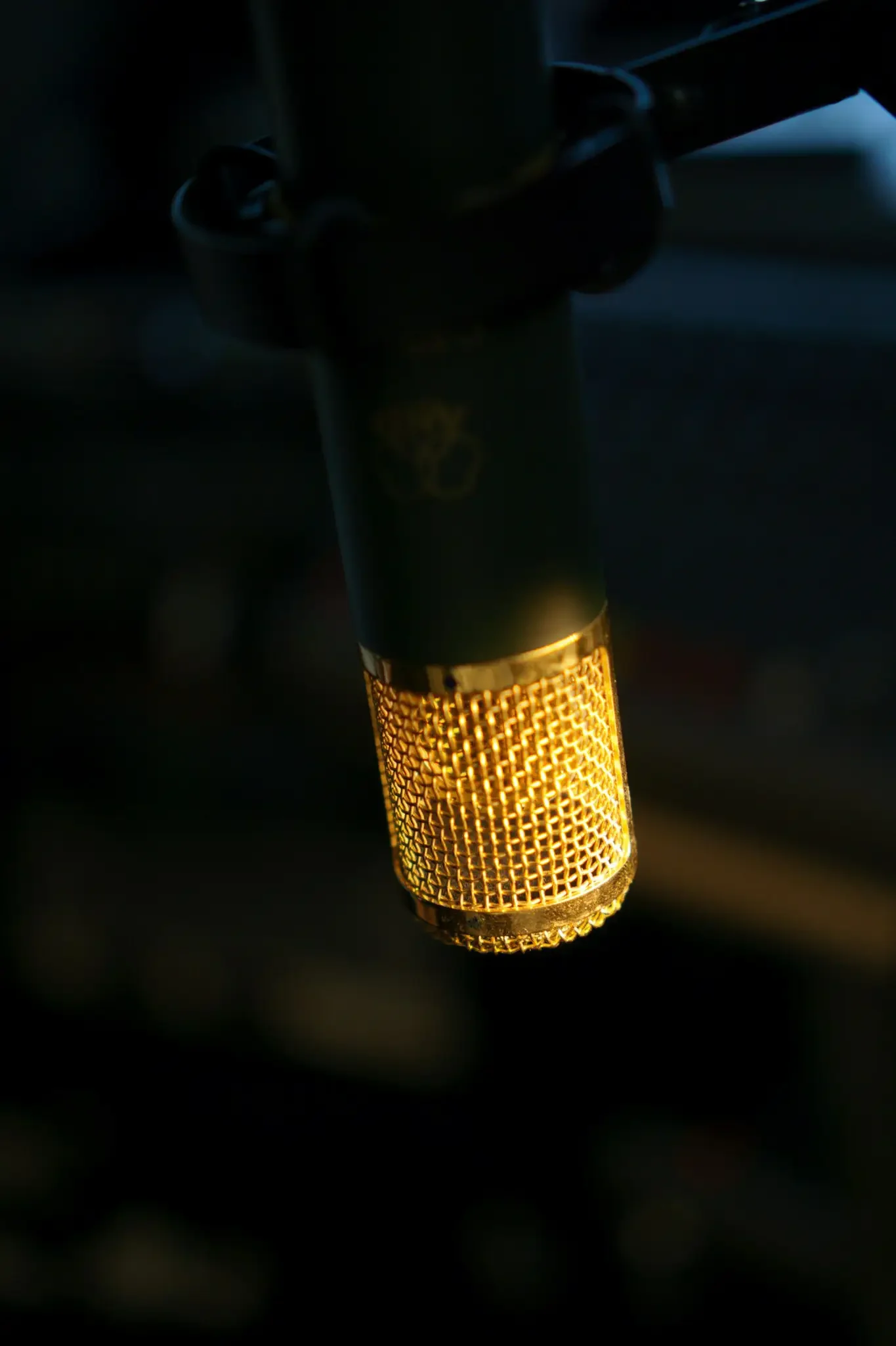 A close-up of a vintage microphone with gold accents, illuminated against a dark background.