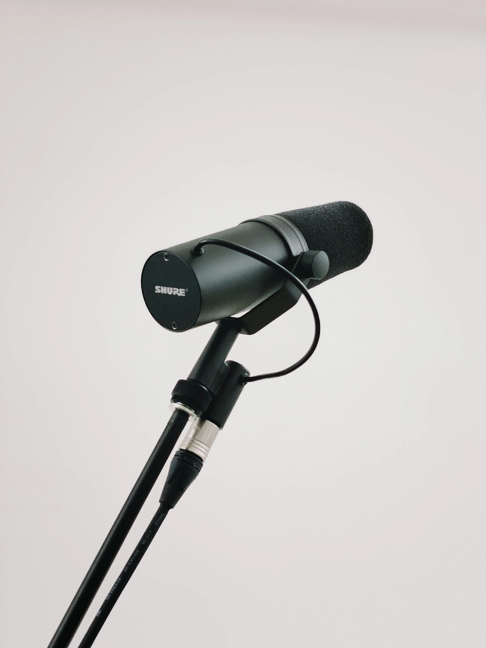 A professional microphone mounted on a stand against a plain white wall.