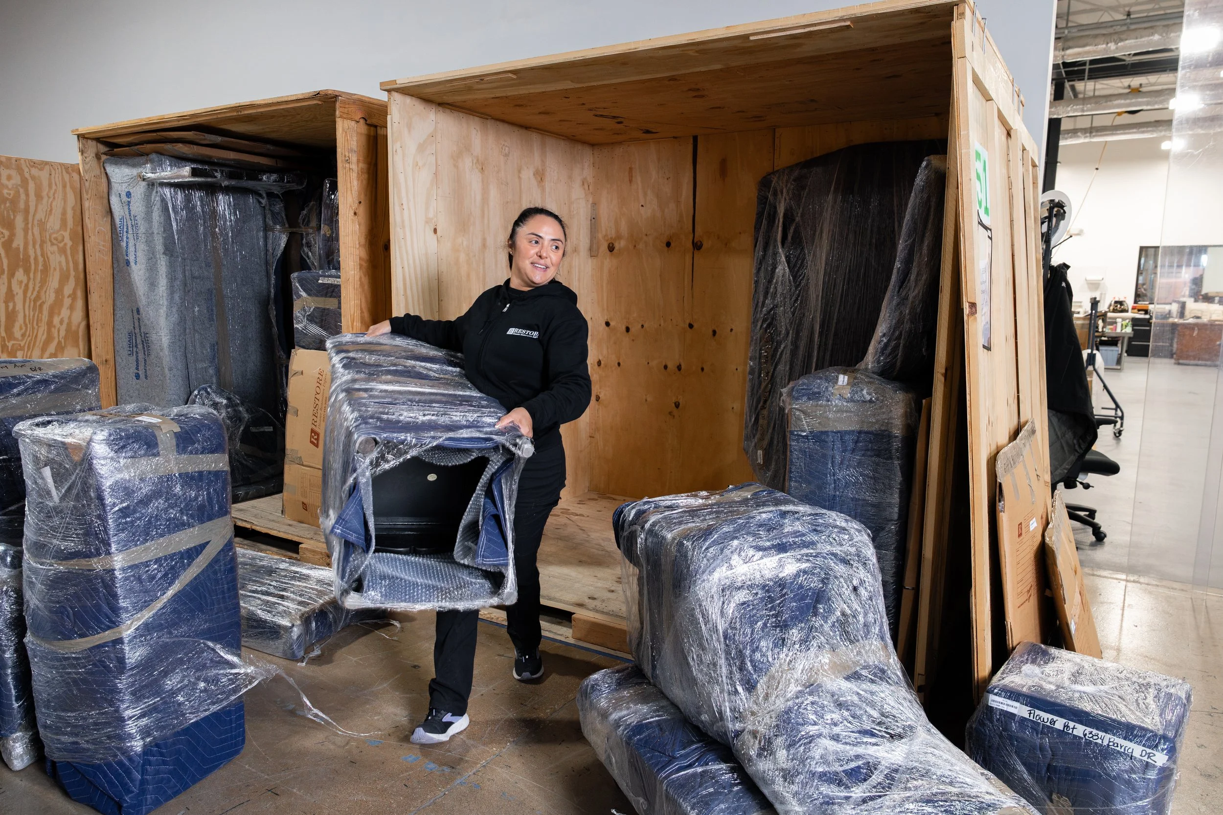 A woman is moving wrapped furniture and boxes inside a warehouse or storage facility.