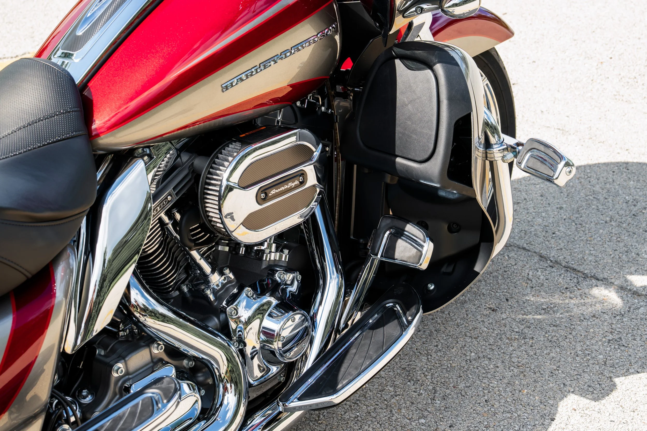 Close-up of a red and gold Harley-Davidson motorcycle showing the engine, foot pedals, and part of the seat on a paved surface.