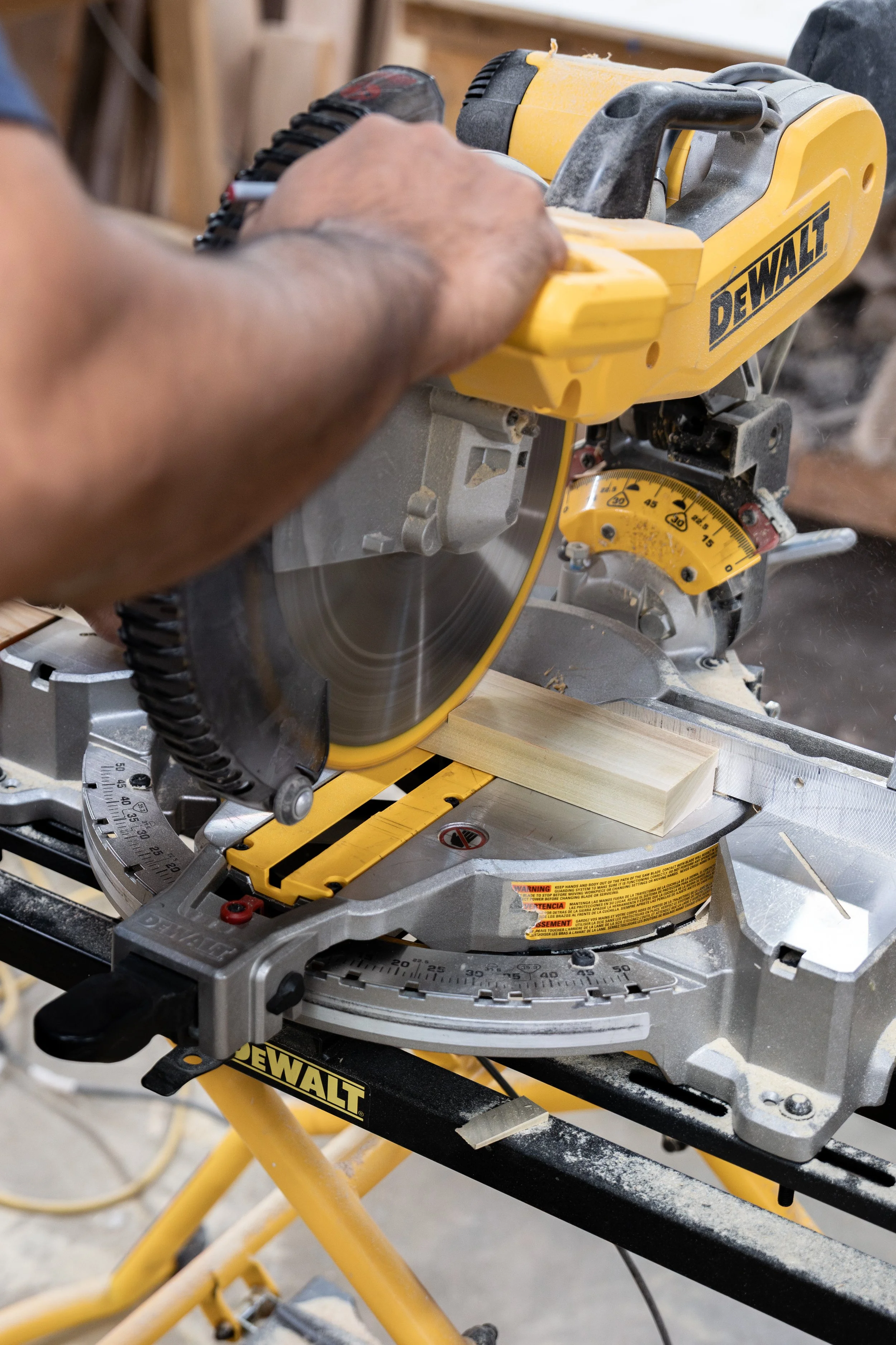 A person operating a yellow DeWalt miter saw to cut a piece of wood. The saw is on a portable stand with measurement markings.