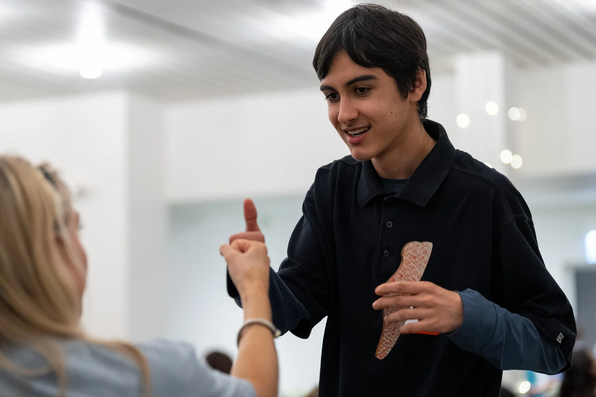 A young man with dark hair smiling and giving a thumbs-up to a woman with blonde hair who is handing him a bandage.