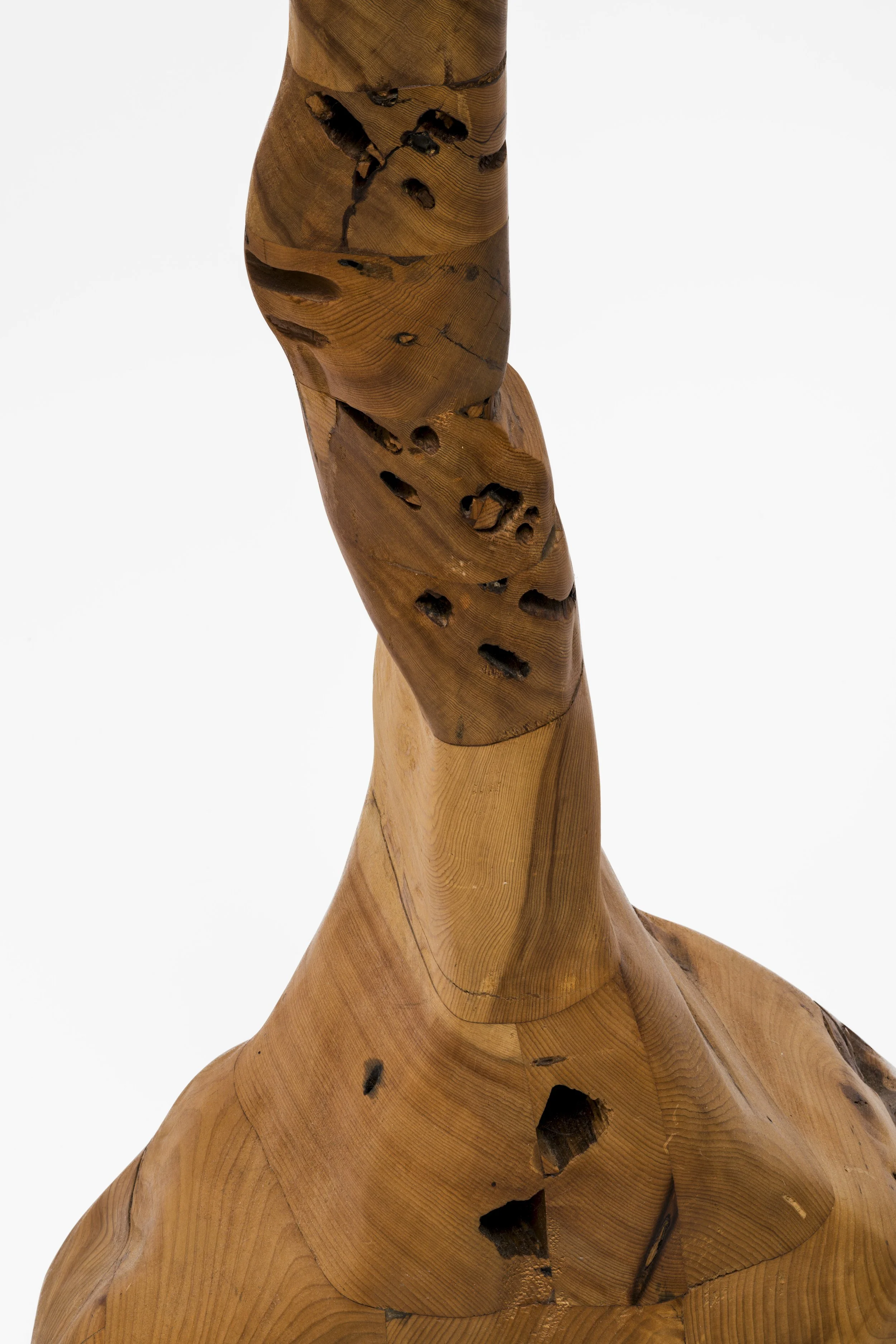 Close-up of a wooden sculpture with a twisted, abstract form and visible wood grain, set against a plain white background.