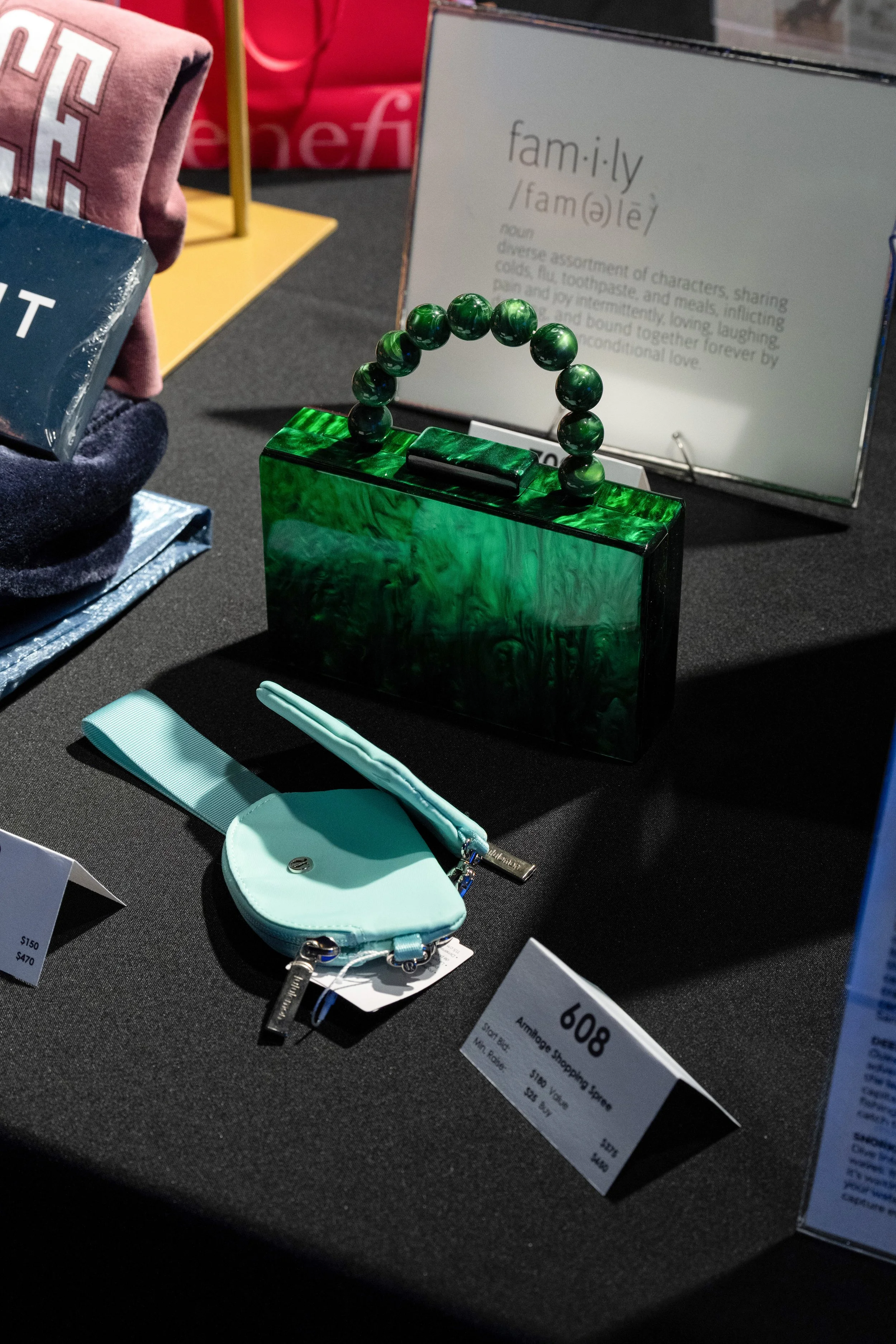 A green handbag with a pearl handle, a small light blue purse, and a sign describing the definition of 'family' with other merchandise in the background.