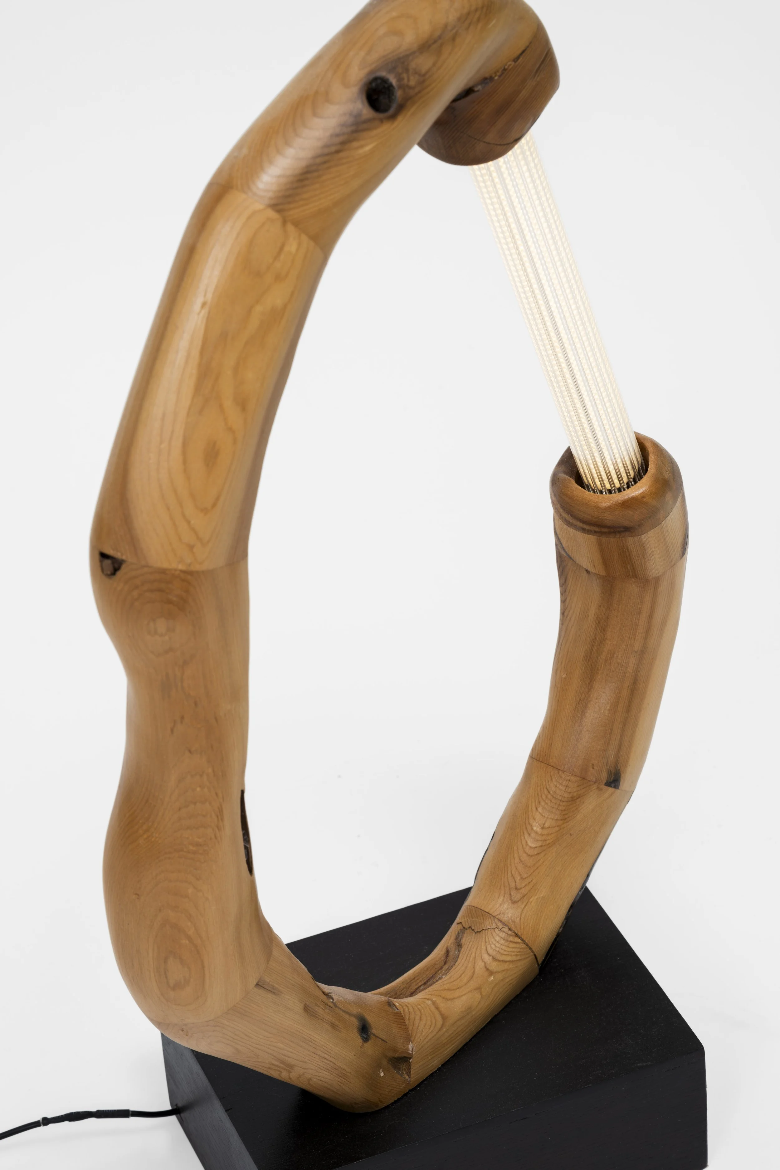 A lamp with a ring-shaped wooden frame, a black base, and a white light strip running through the center.