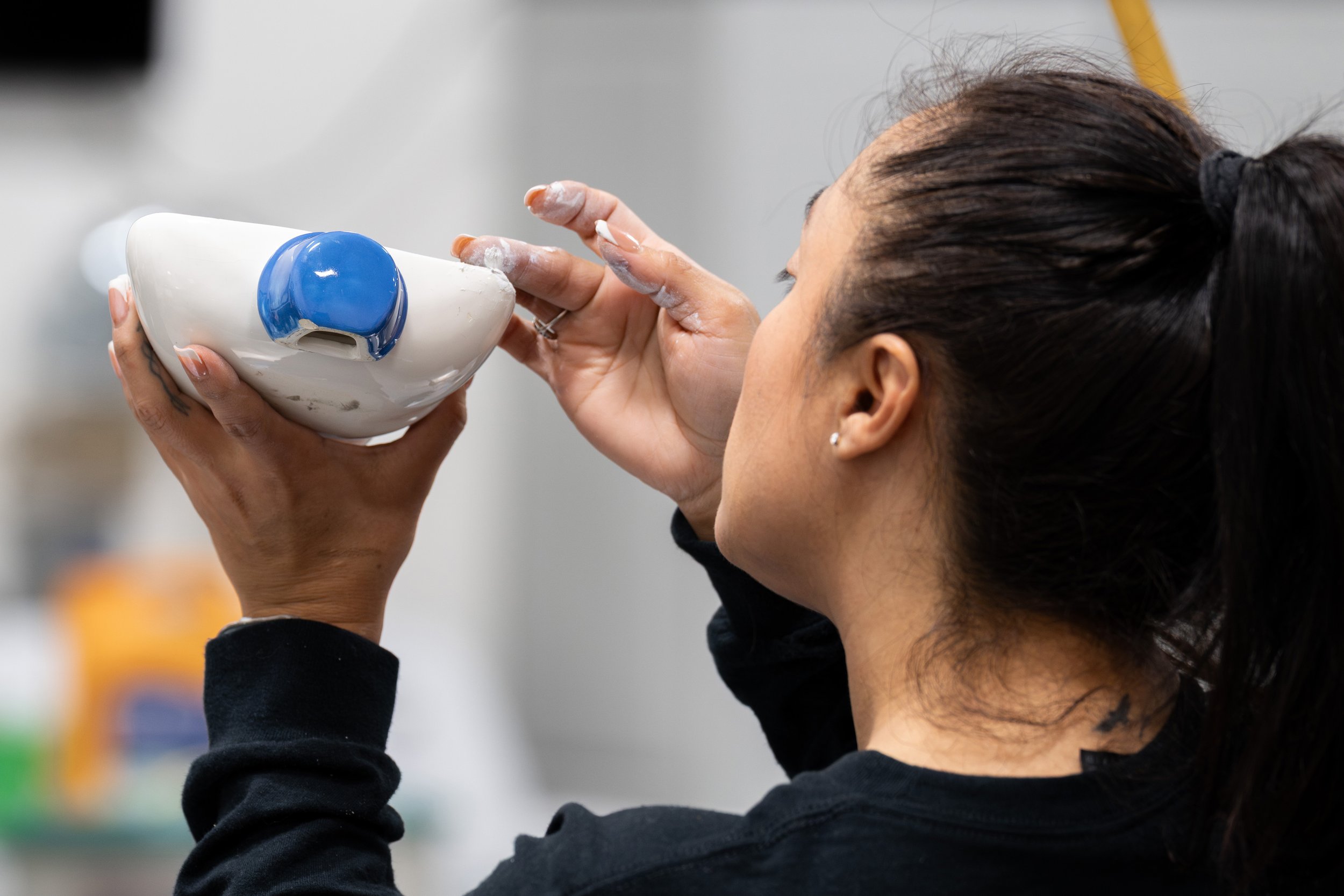 A woman with dark hair tied back, holding a white bowl with blue markings and drinking from it.