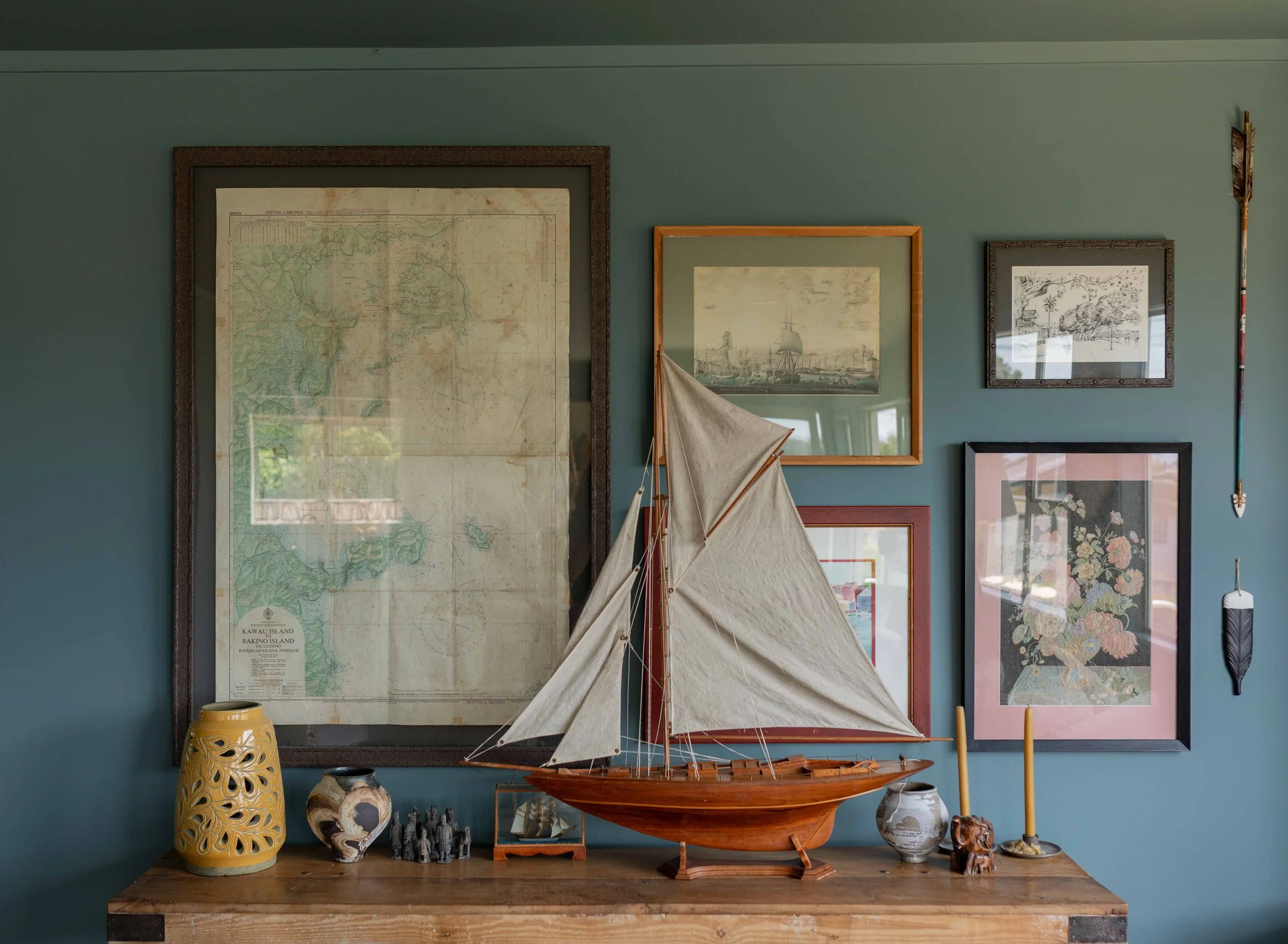 Gallery wall with vintage artwork, vintage console on which sits vintage ship, vases, candlesticks and decor.