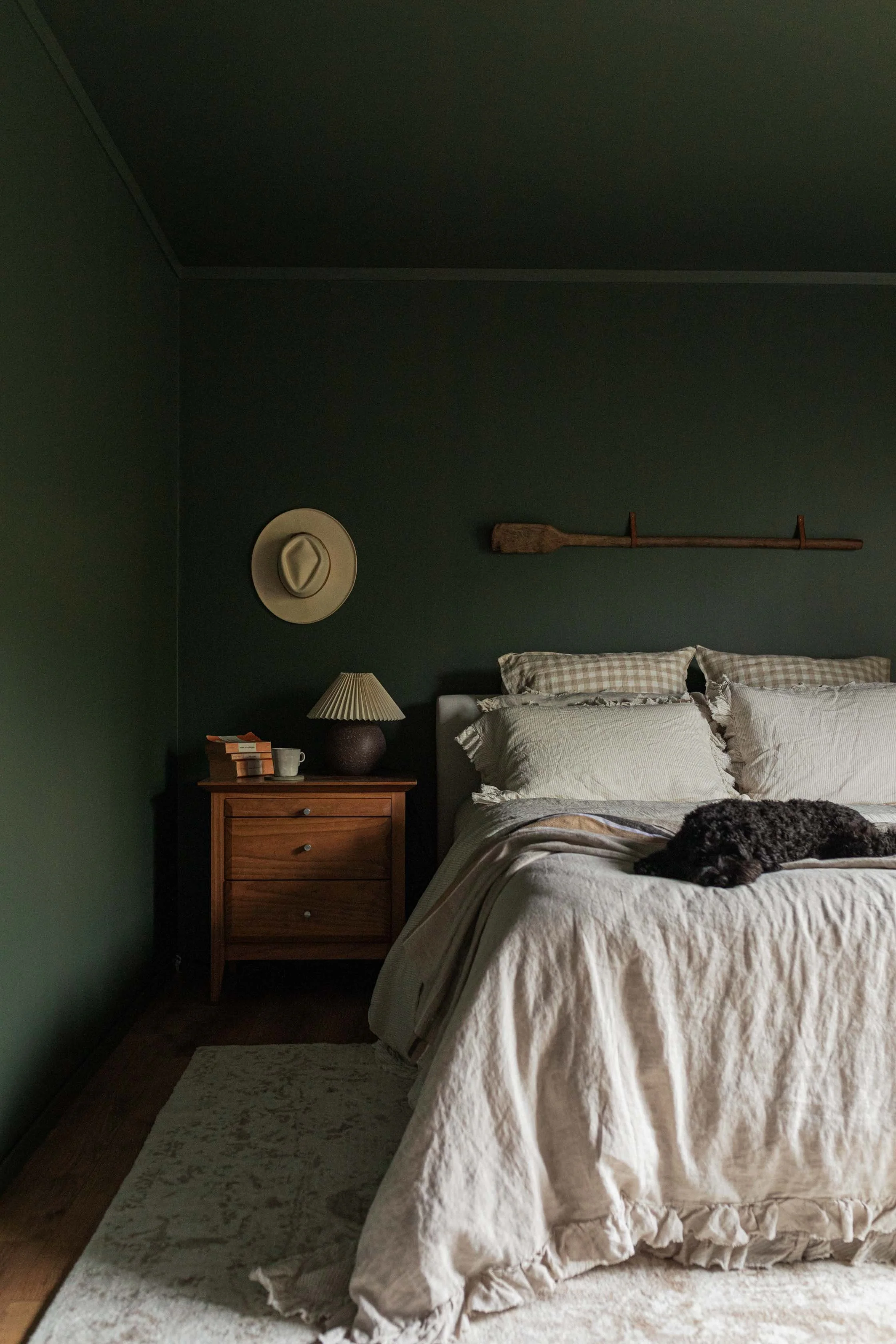 small_black_dog_resting_on_bed_wrinkled_moody_guest_bedroom.jpg