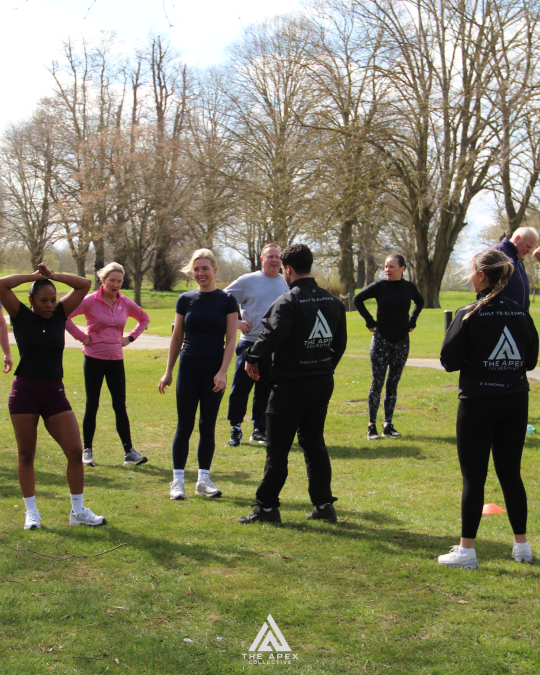 Group of people participating in outdoor fitness training session on a grassy field with trees in the background.