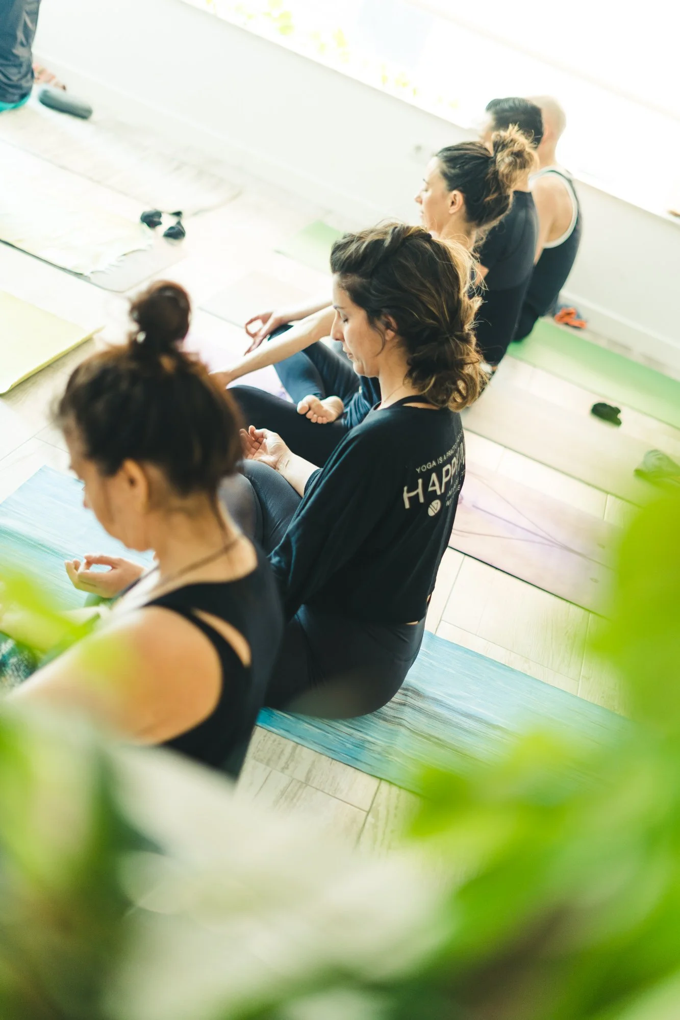 Grupo de mujeres participando en una clase de yoga en interiores, sentadas en colchonetas en posición de meditación.