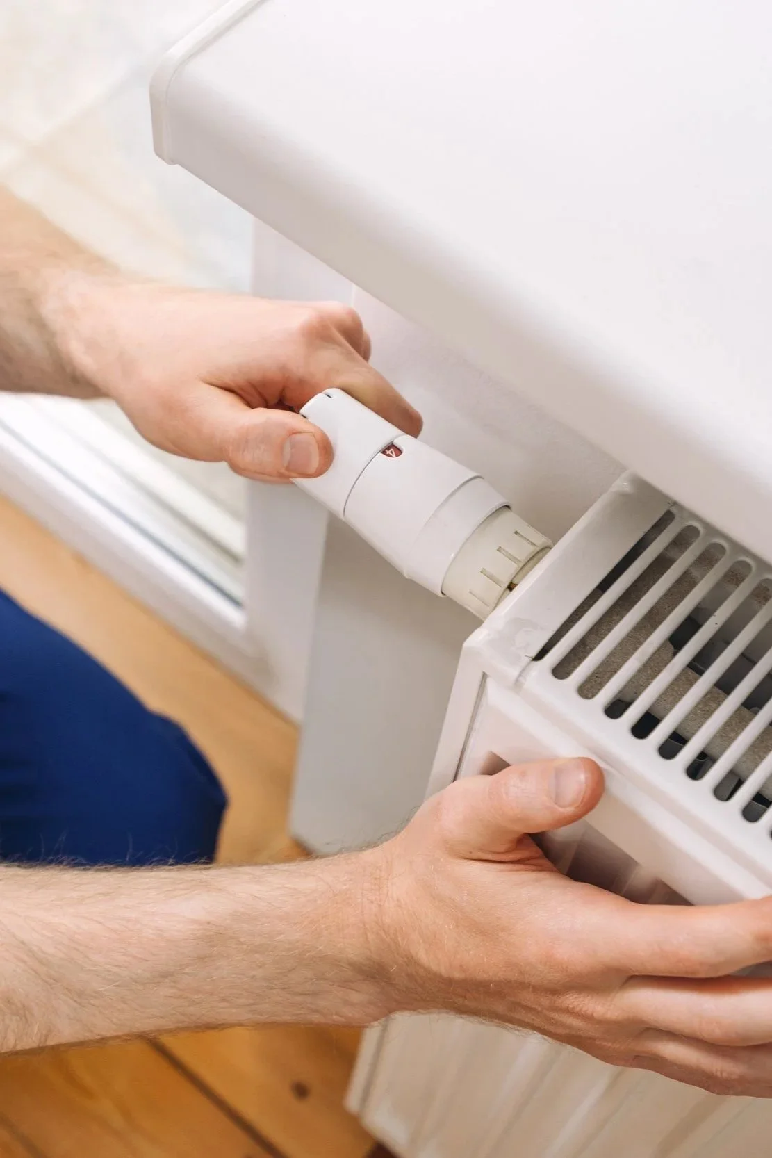 Close-up d'un électricien réglant un radiateur électrique à l'aide d'un thermostat.
