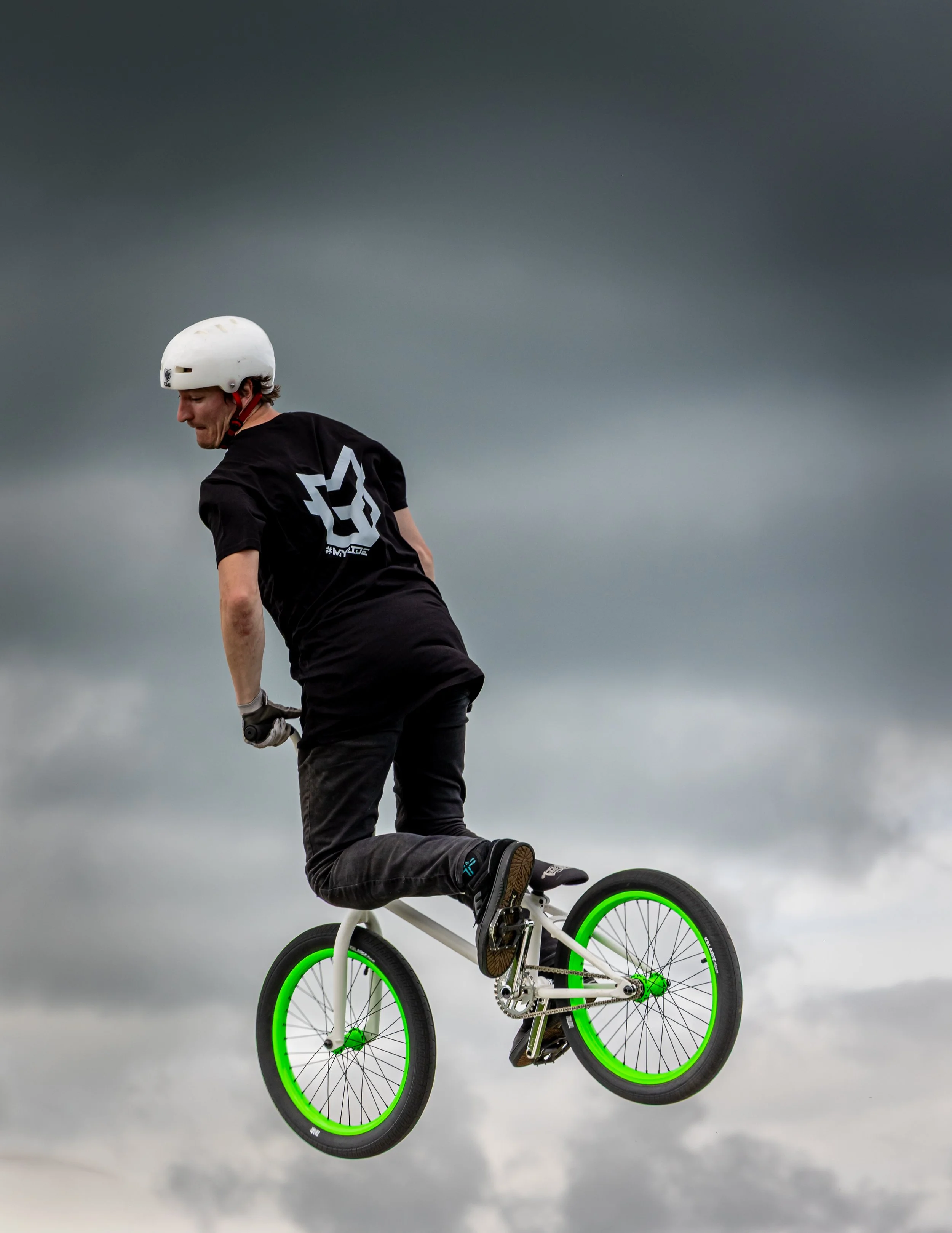 A person riding a BMX bike in the air against a dark, cloudy sky.