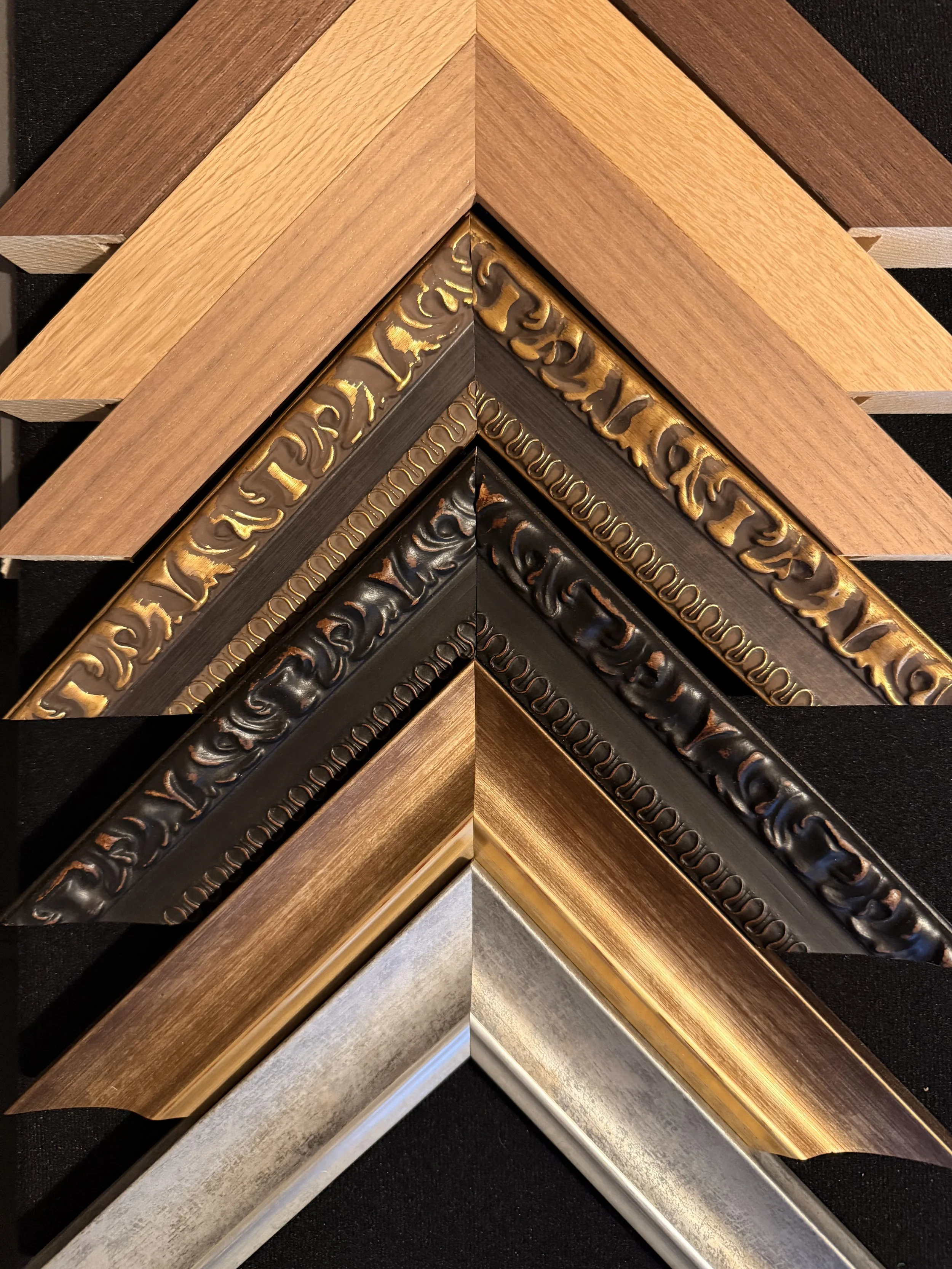 An assortment of picture frames in various metallic and wooden finishes arranged in a layered manner.
