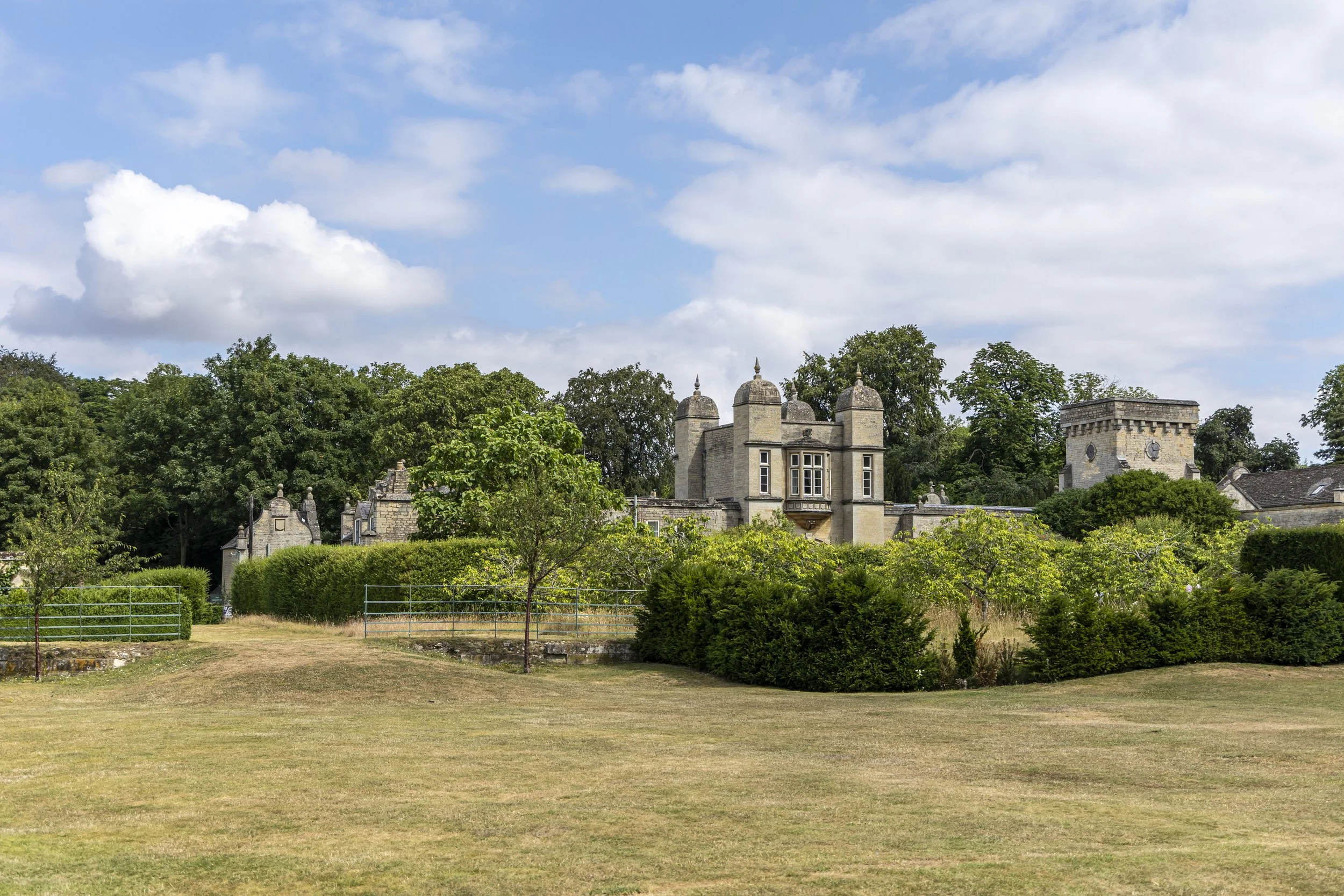 A historic stone building with turrets and a clock, surrounded by trees, under a partly cloudy sky.