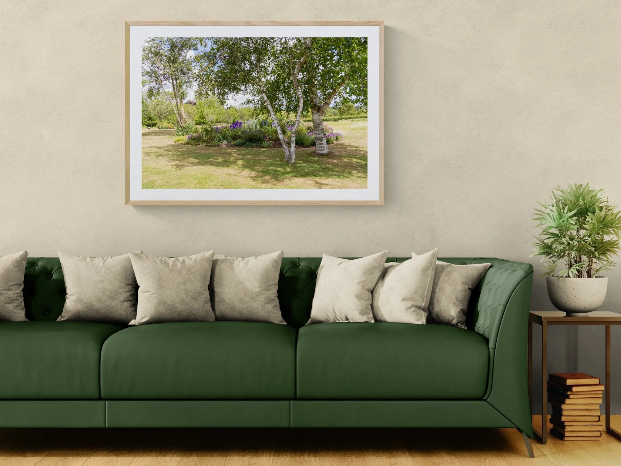 Living room with a green sofa, beige walls, a framed landscape photo, a side table with books, and a potted plant.