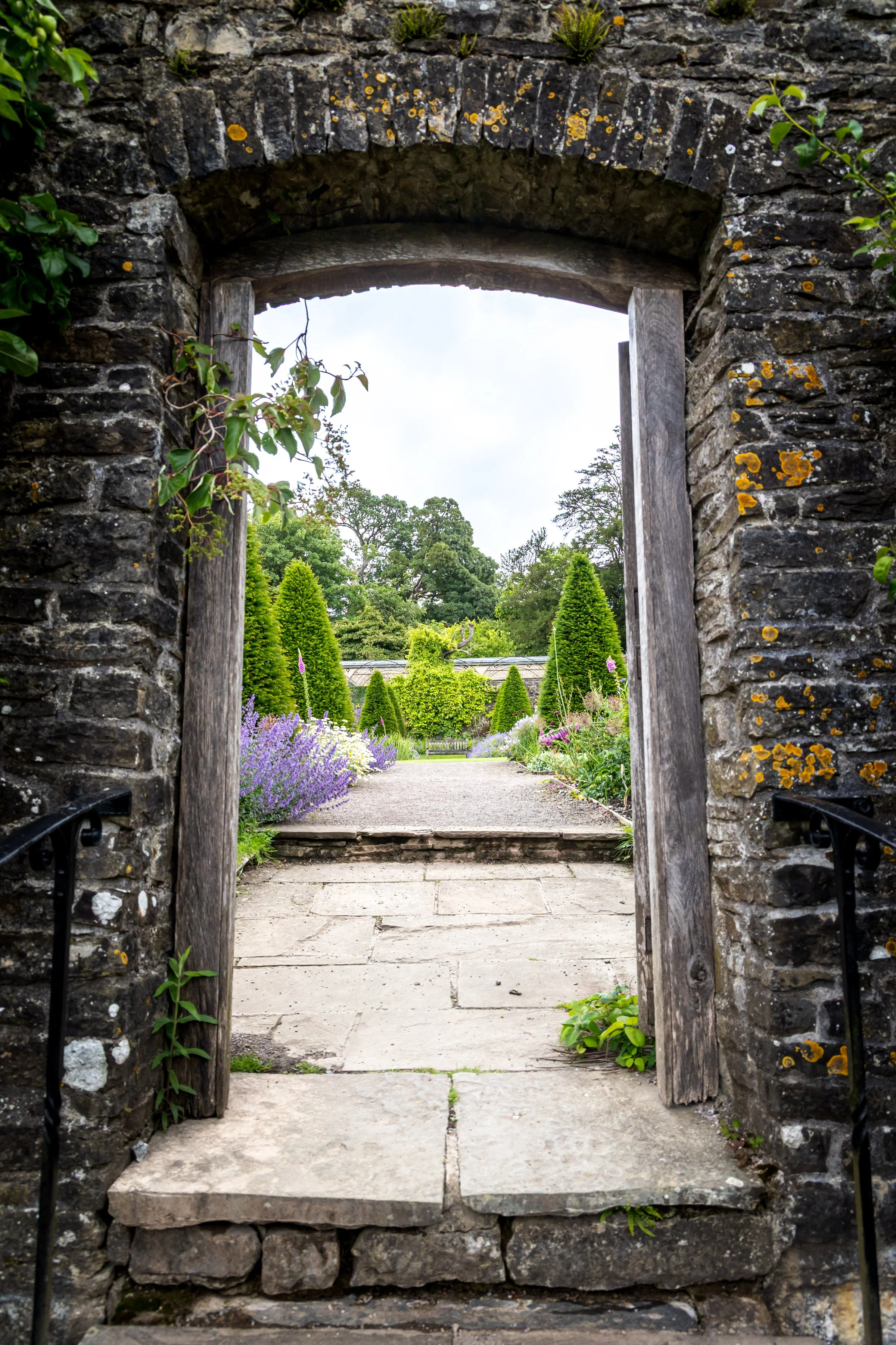 Stone arch doorway leading to a garden with lush green plants and topiary trees.