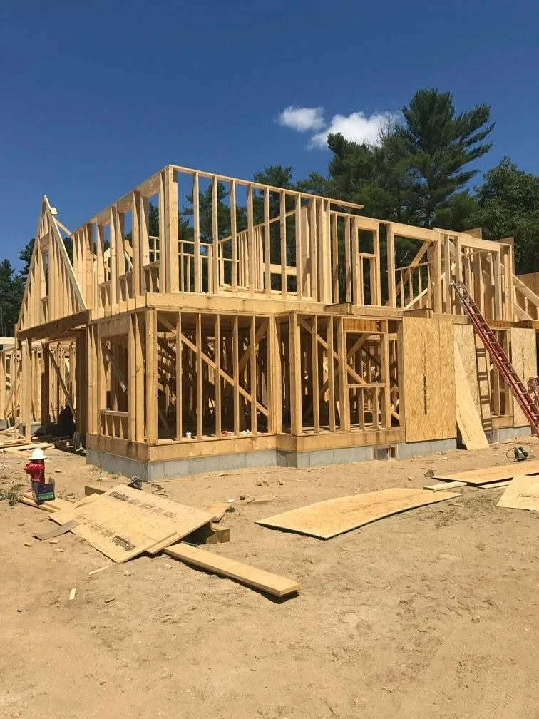 Wood framing of a house under construction with blue sky and trees in the background.