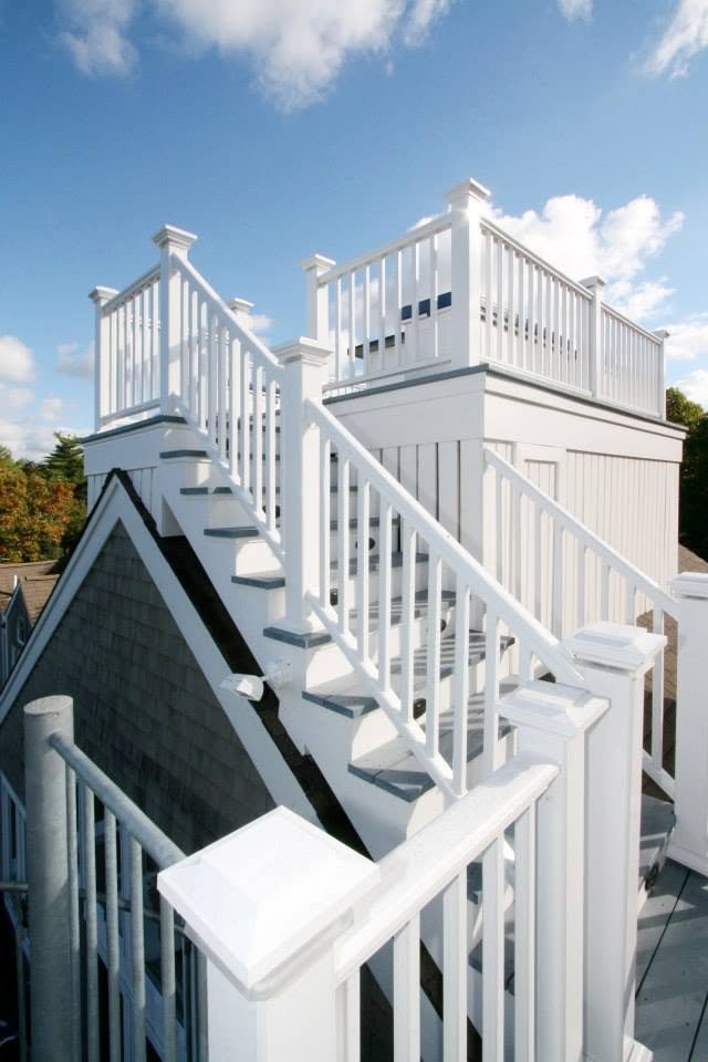 White wooden rooftop deck with stairs and railing, under a partly cloudy sky.