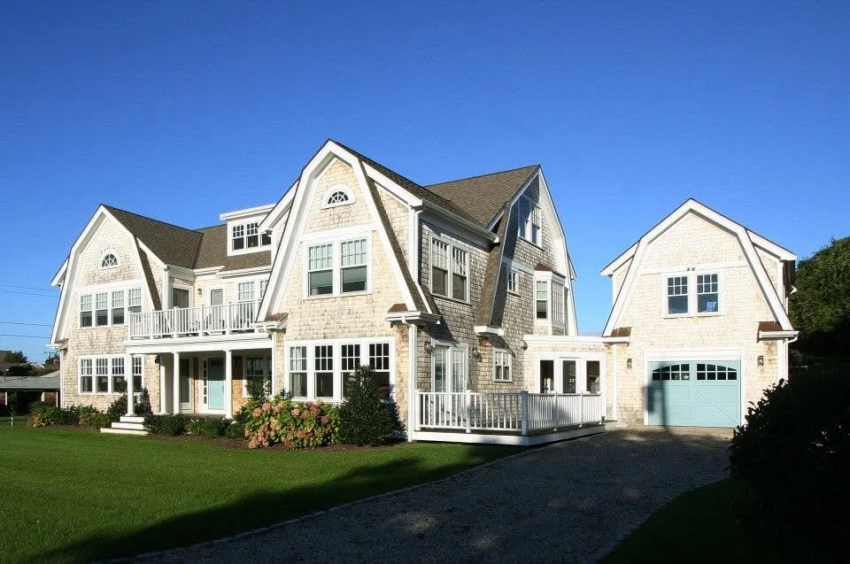Large modern house with multiple peaked roofs, a garage, and a landscaped front yard under a clear blue sky.