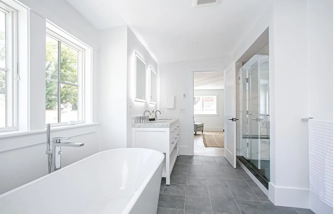 Modern bathroom with a freestanding bathtub, double vanity sinks, a glass shower enclosure, and large windows with a view of trees outside.