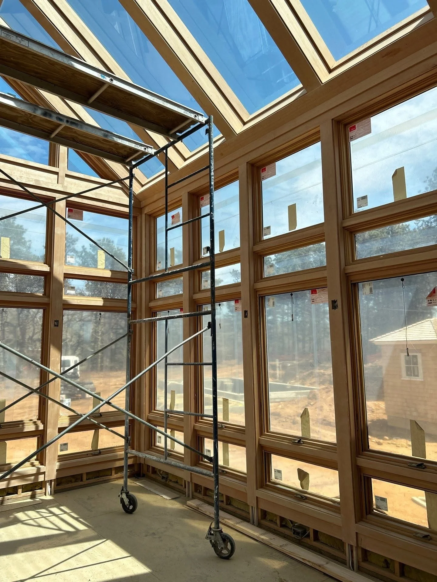 Interior of a building under construction with large wooden-framed windows and skylights, and a scaffolding tower inside.