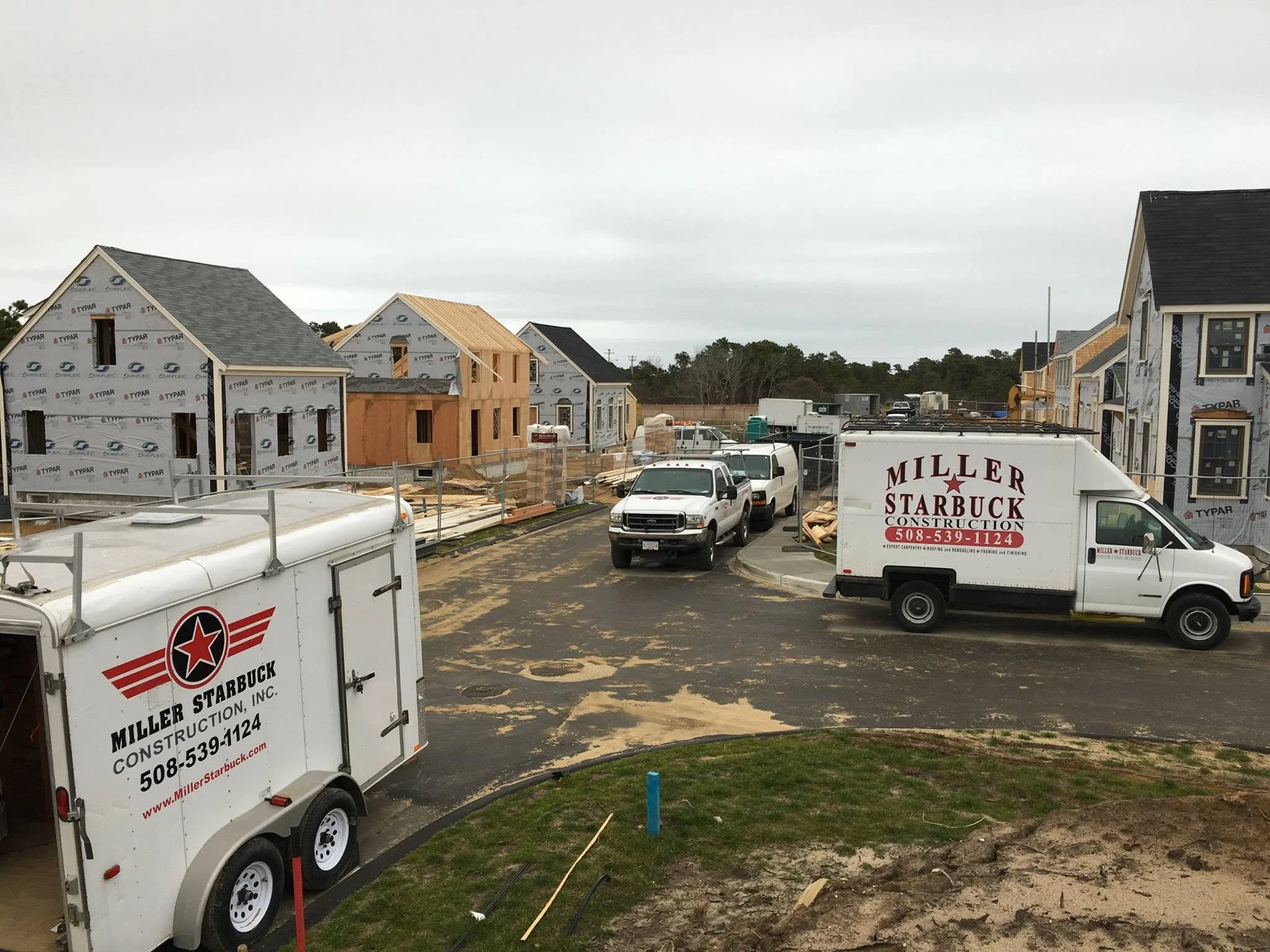 Construction site with houses under construction, parked Miller Starbuck Construction trucks, and building supplies.