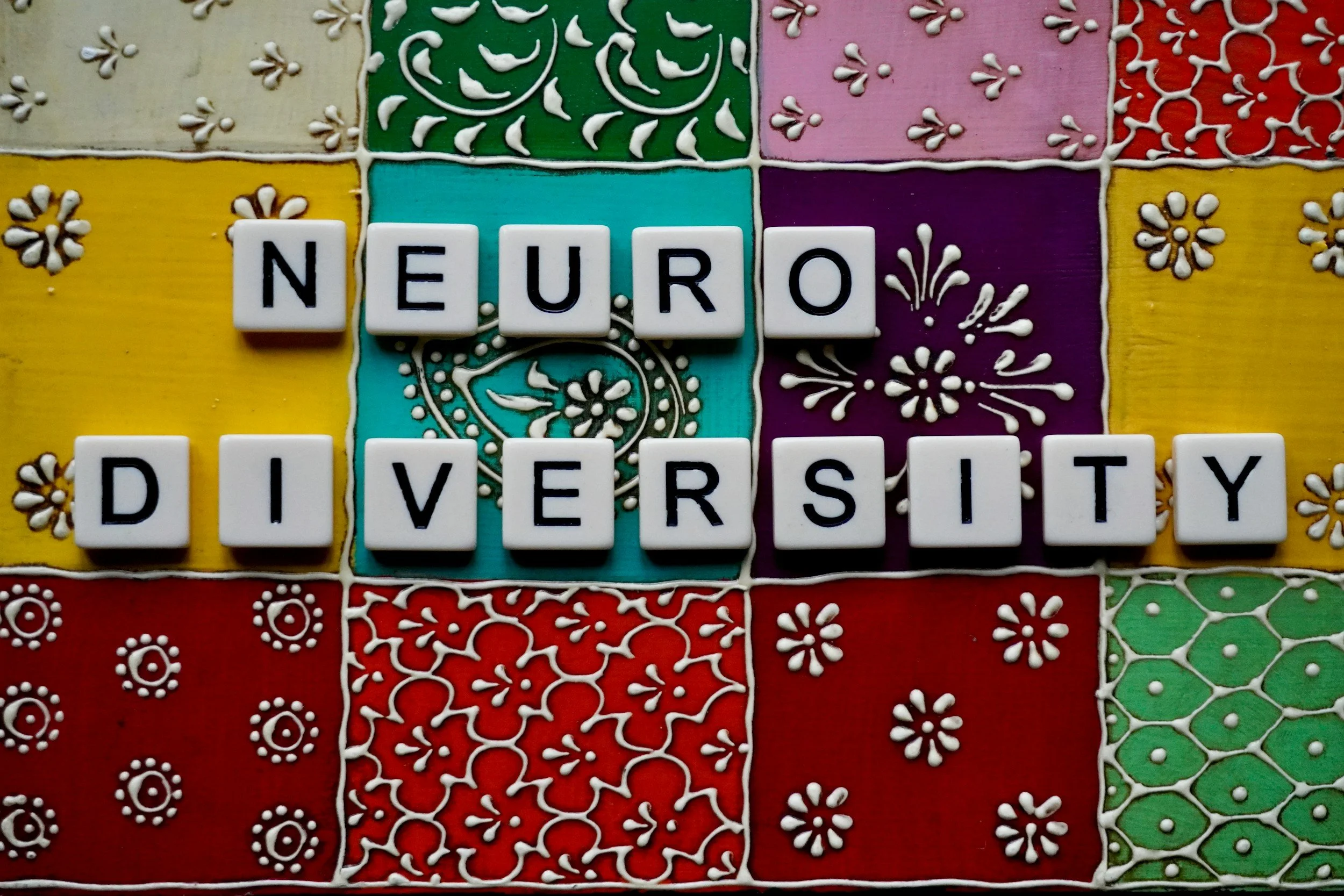 Scrabble tiles spelling 'NEURO DIVERSITY' on a colorful, decorative background.