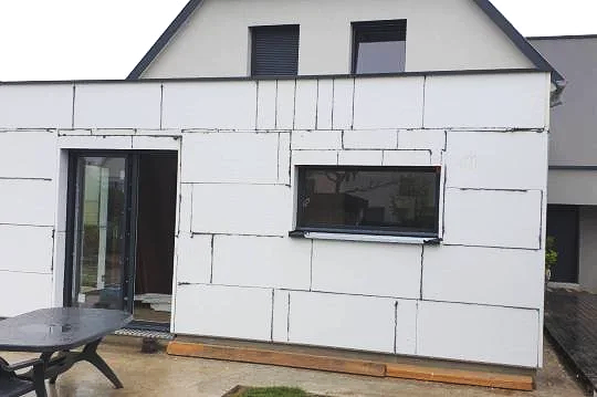 Une extension en construction d'une maison avec des murs en isolation ou en cloisons en béton blanc.