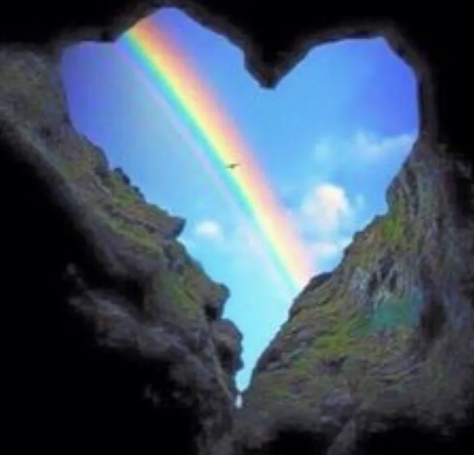 Rainbow across a blue sky through a rock cave shaped like a heart