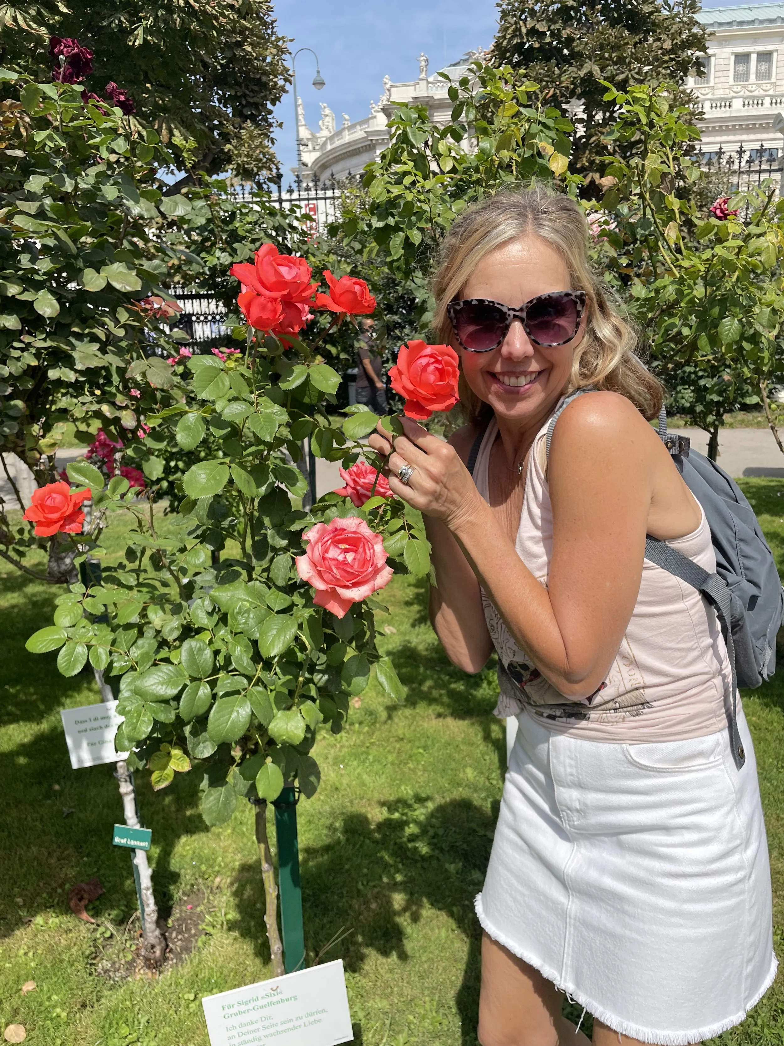 Kirsten Nelson Telan standing outside posing alongside a vibrant rosebush with red pink flowers