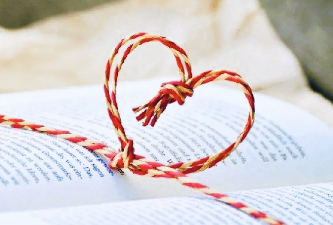Red and white string tied into a knot with a heart over an open book