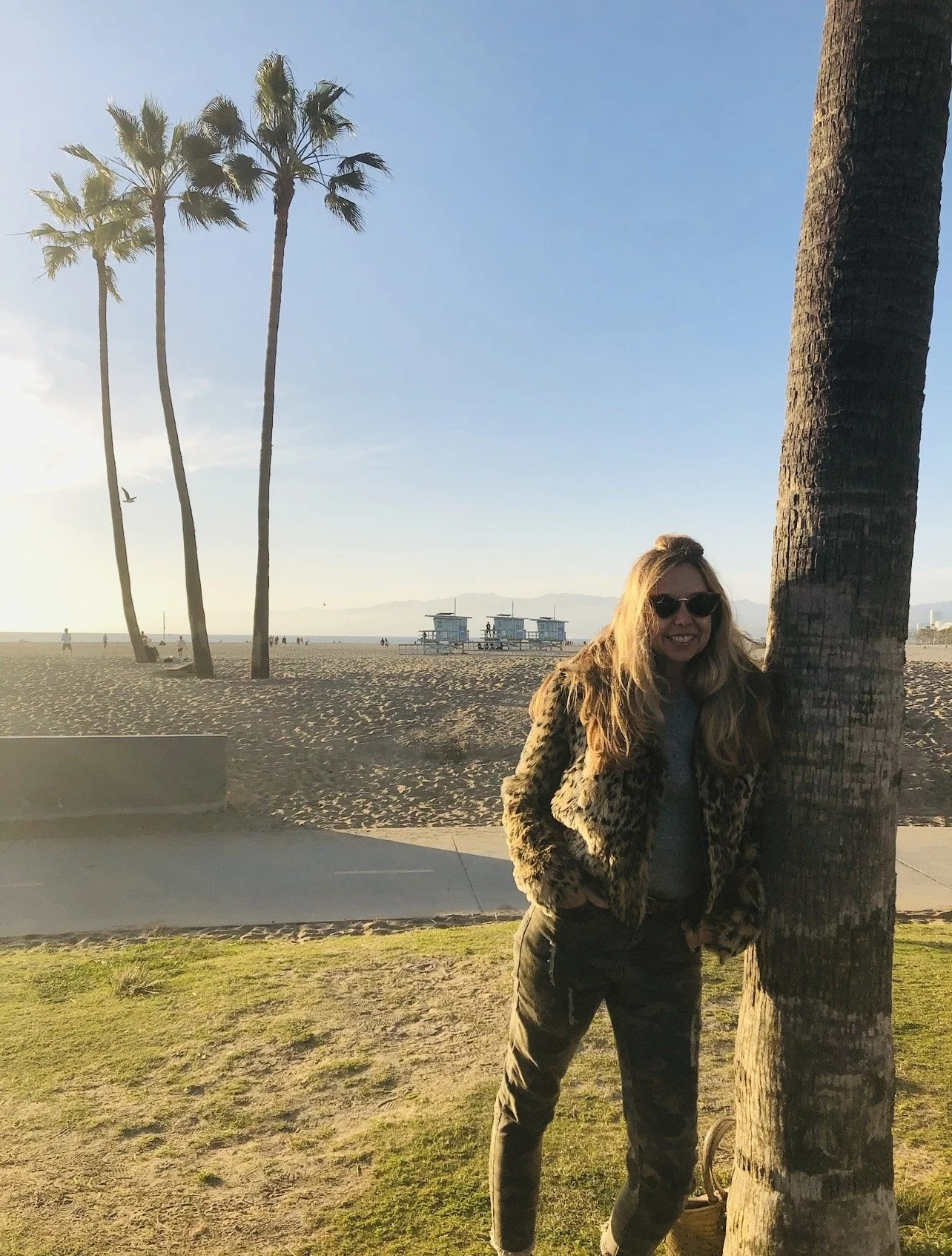 Kirsten Nelson Telan standing against a plan tree with a sunny, blue, clear sky and tall palm trees on the beach in the background in Florida