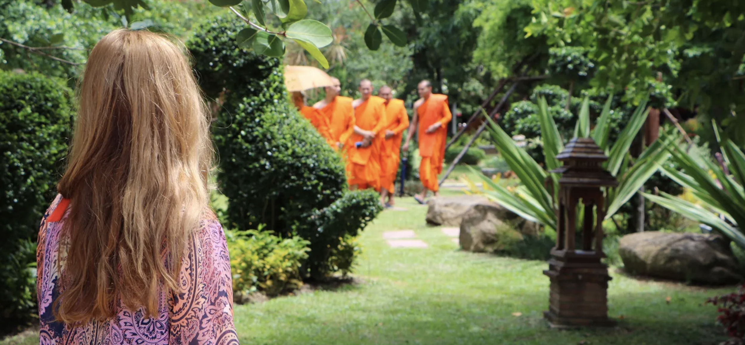 International traveling photo of a green outdoor area with a group of men, or monks, walking together and a woman watching from a distance