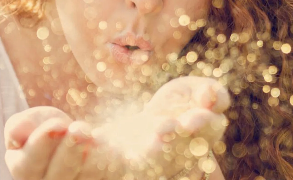 Woman blowing a handful of sparkles into the camera