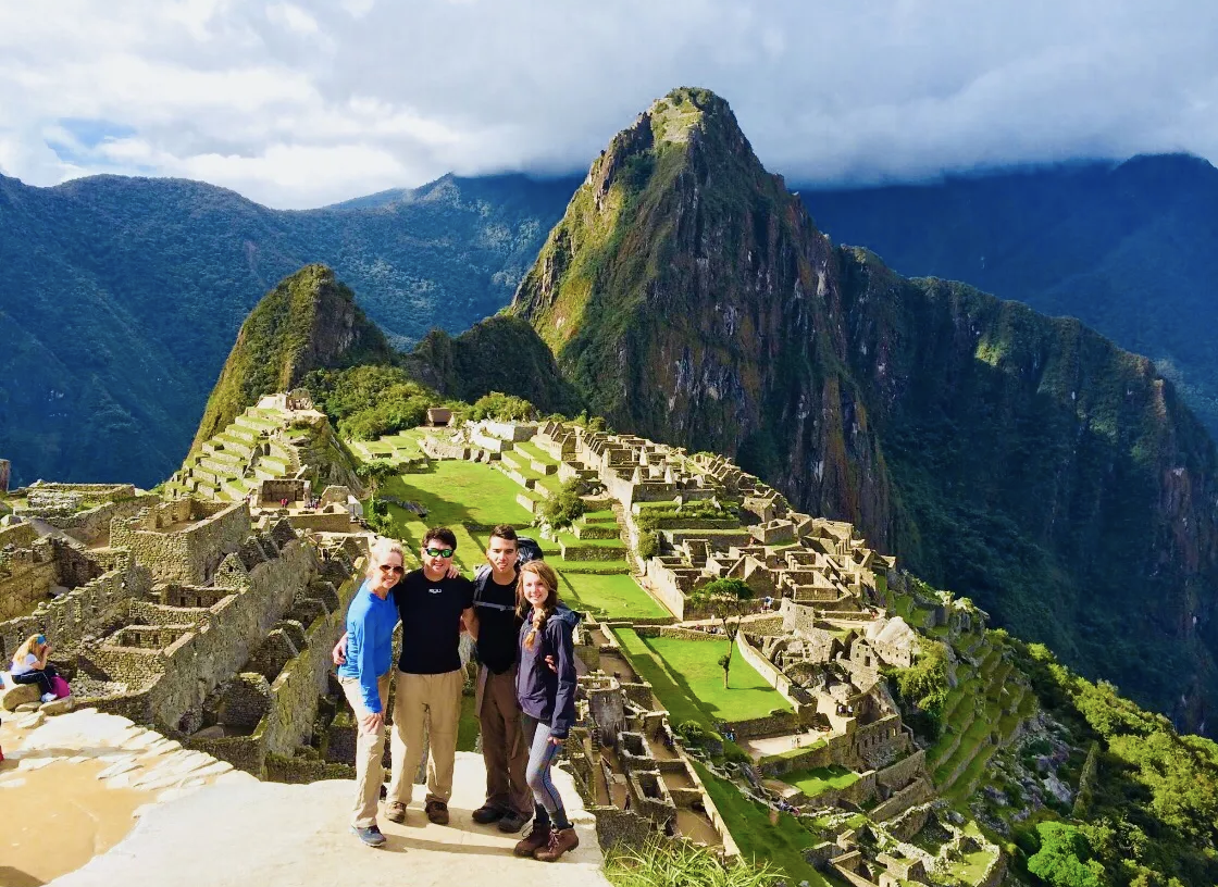 Kirsten Nelson Telan's family travling internationally posing in front of a large green mountain range and ancient rock village