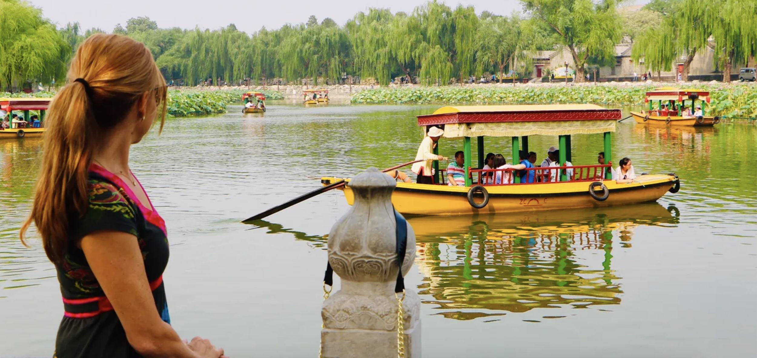 International travel photo of a lake with colorful boats and a woman watching from afar
