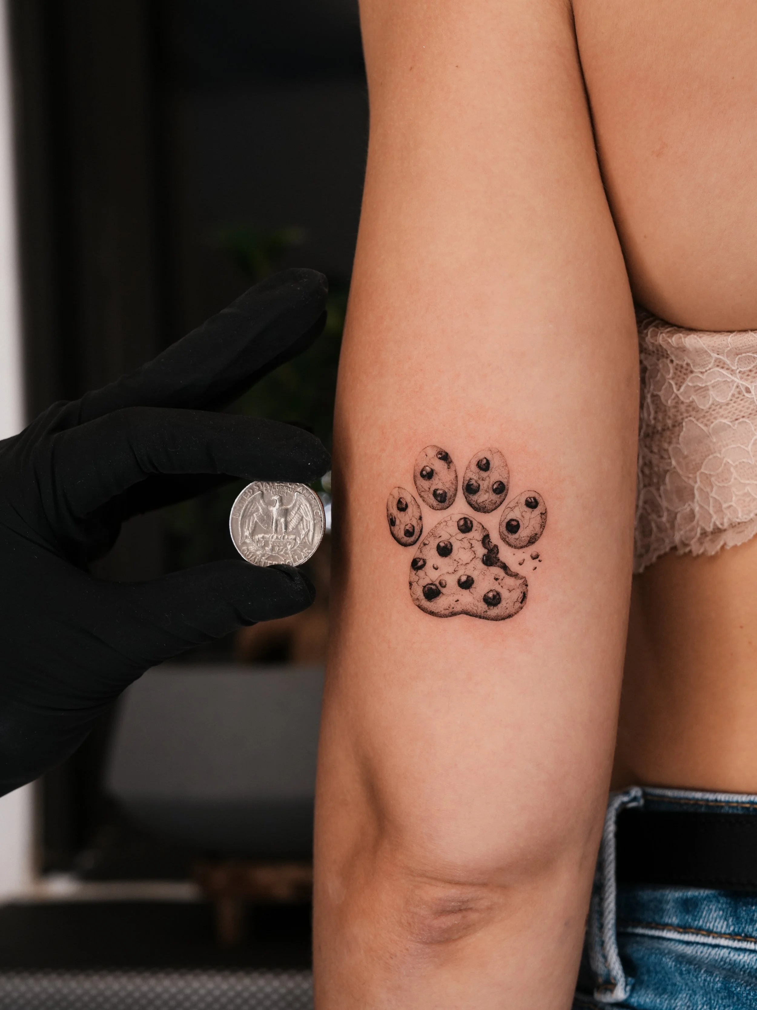 A tattoo of a puppy paw print illustrated with chocolate chip cookie pattern on a person's upper arm. Done by famous tattoo artist located in Financial District of New York City - Gregory Mirzoyan @gmtattooing