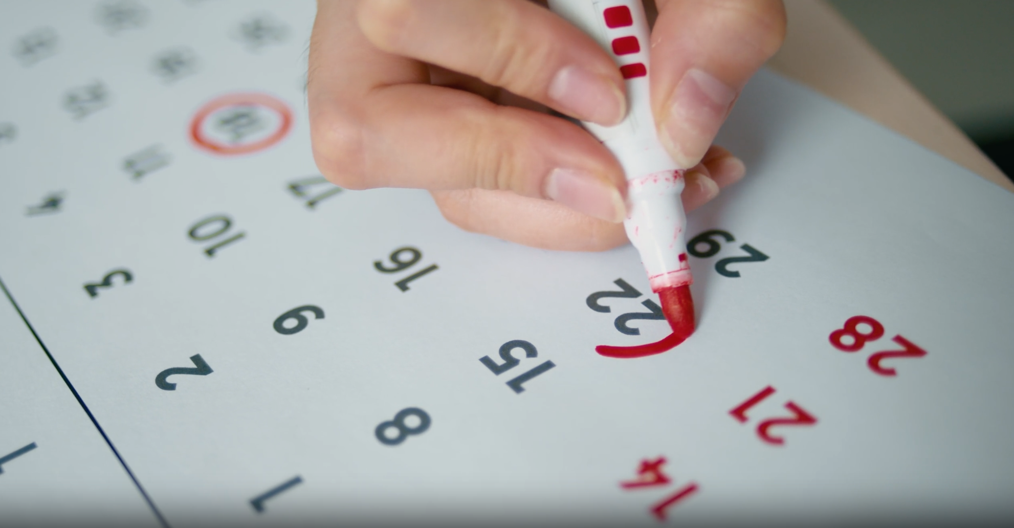 Hand marking a date on a calendar with a red marker.