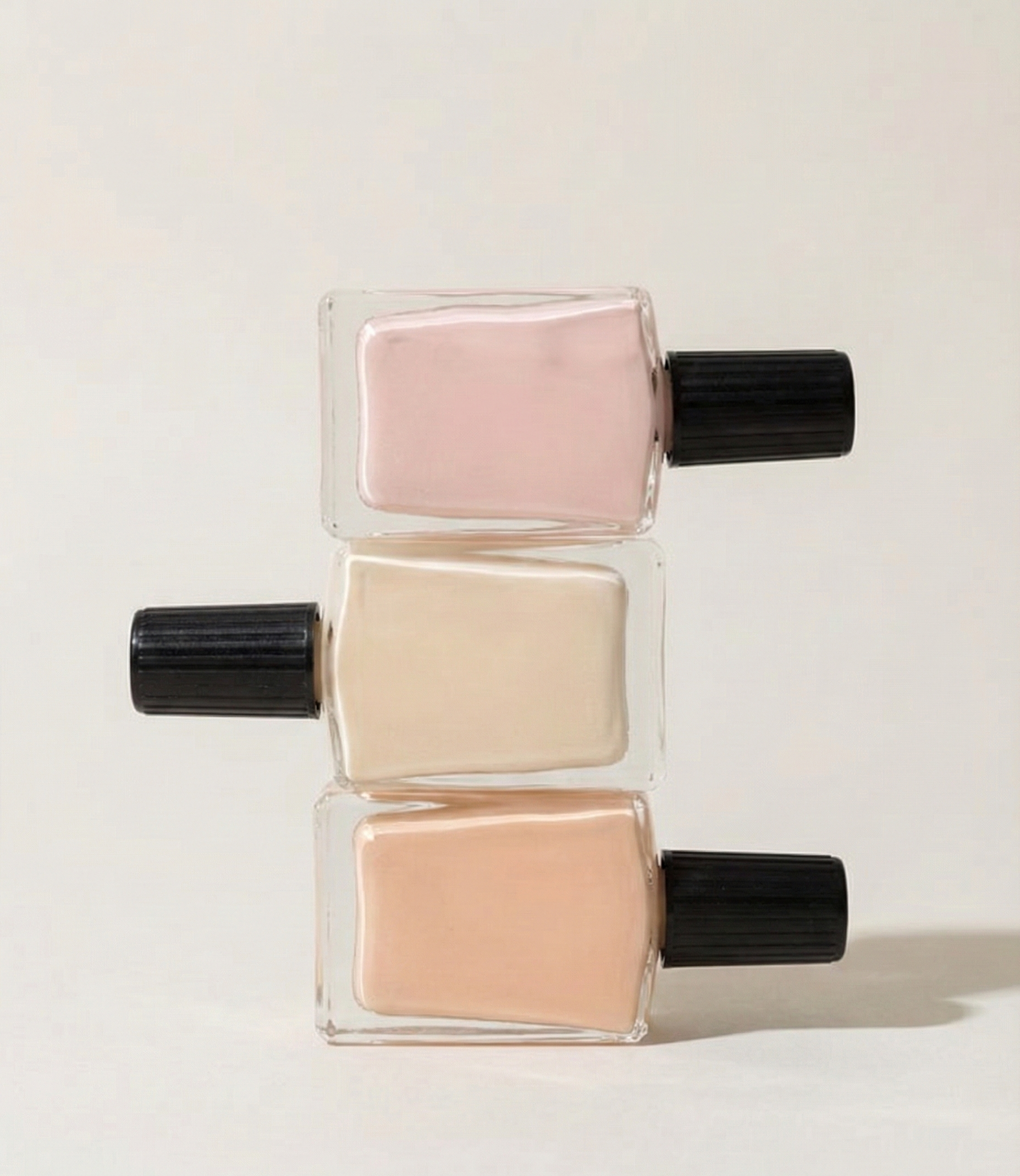 Stacked small glass bottles with black caps containing pastel-colored liquids, arranged vertically on a white background.