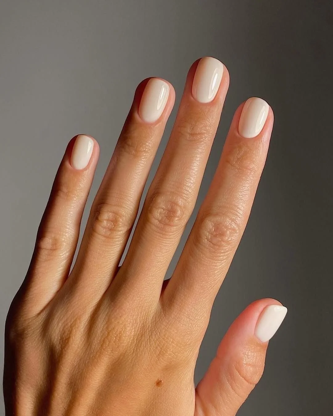 Close-up of a hand with well-groomed nails painted in a light, natural color, set against a neutral background.