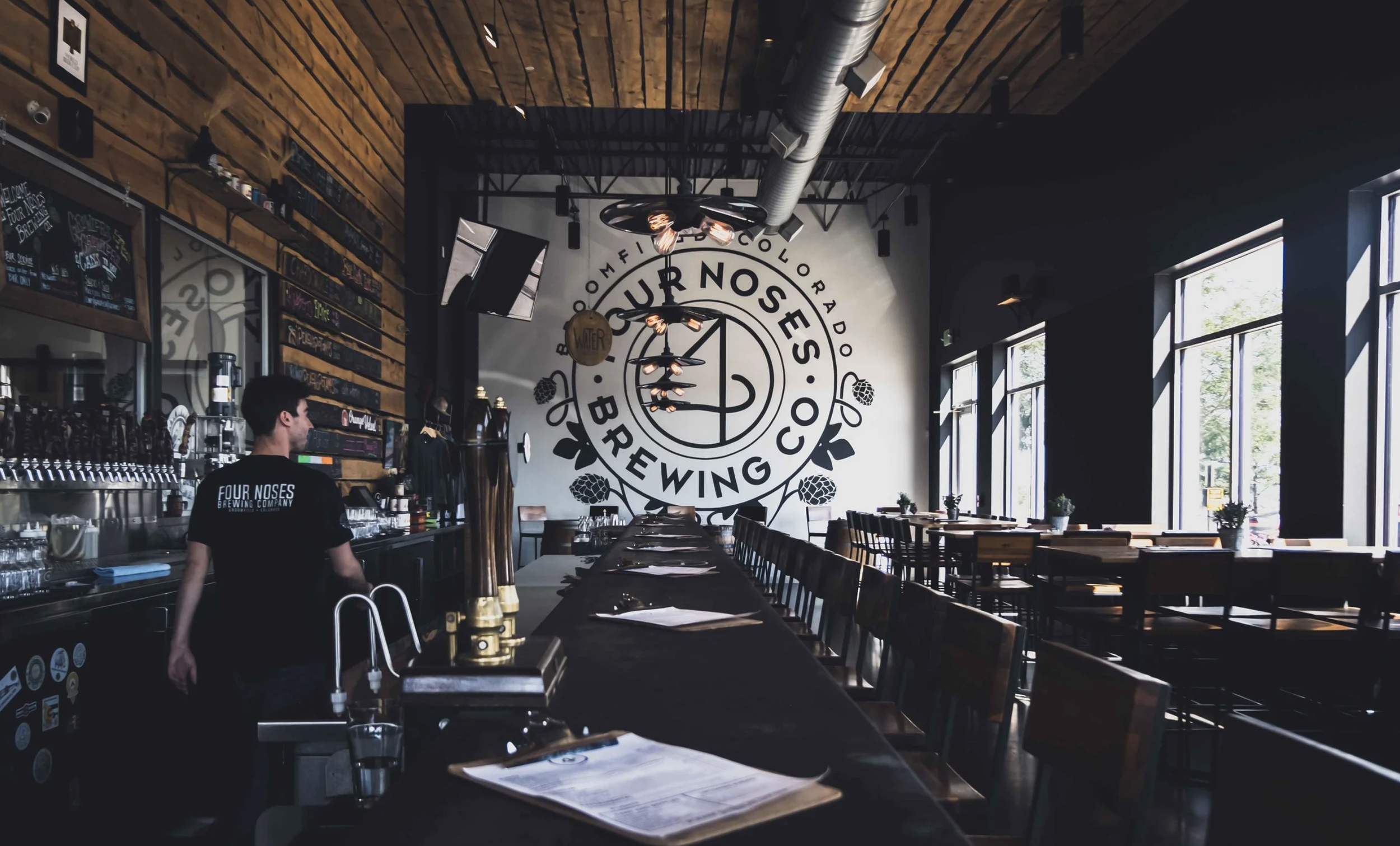 Interior of 4 Noses Brewing Company in Broomfield, Colorado, featuring a long bar, wooden seating, and the brewery’s logo wall