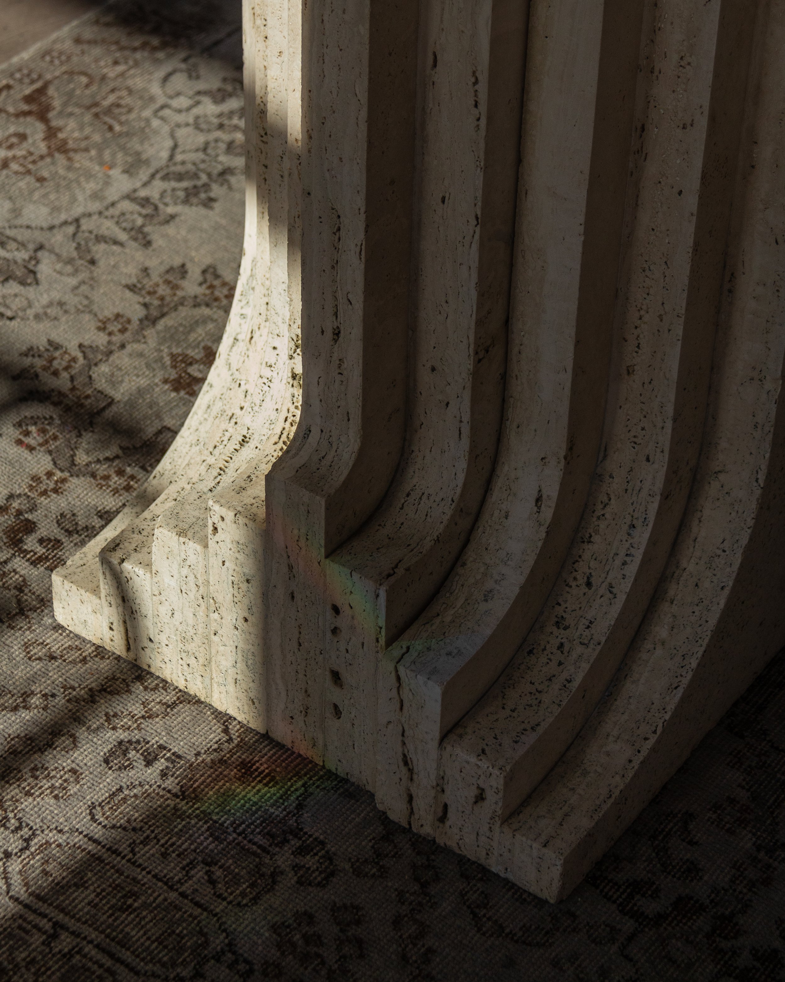 Close-up of a textured stone column base with curved grooves on a patterned rug.
